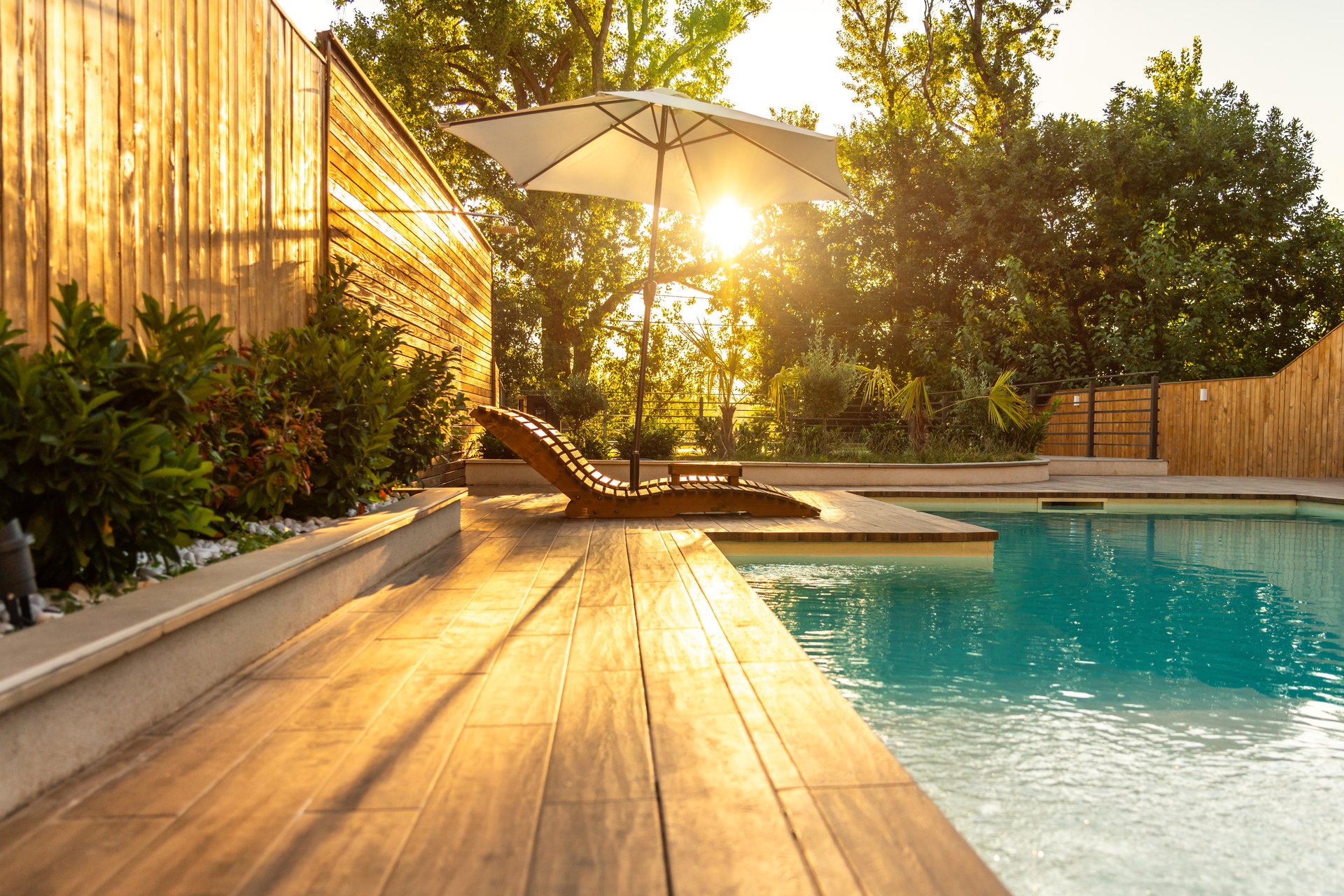 Swimming pool in modern private villa with lounge chairs, palm trees and umbrella at sunset