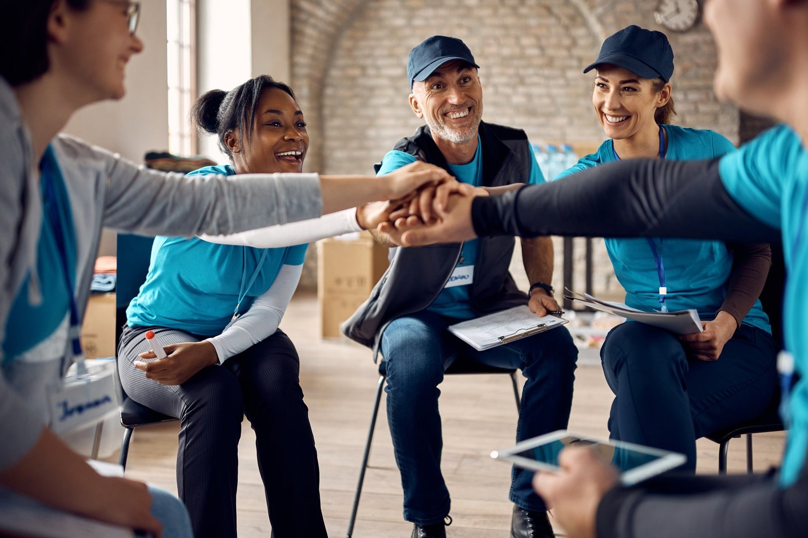 Multiracial group of happy volunteers stacking their hands in unity while working at humanitarian aid center.