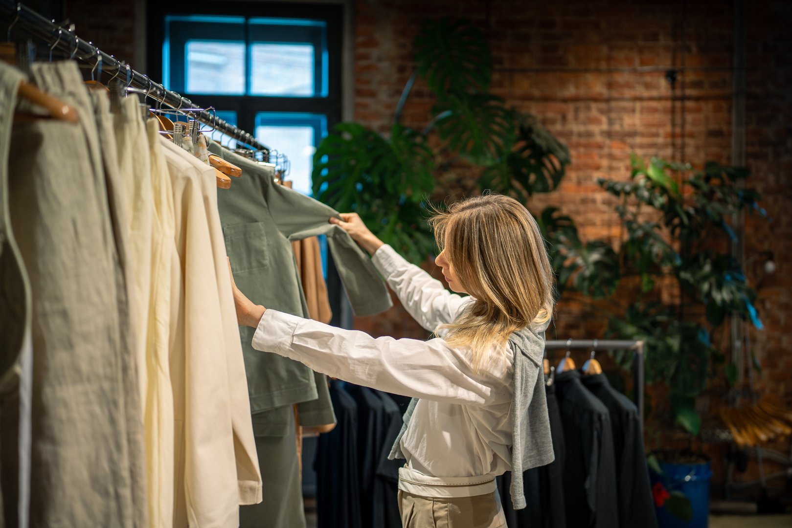 Tranquil female buyer sorting, choosing clothes on rail in dress outlet. Shopping indulgence, leisure in deciding on outfits, Female customer spending money in resale store with hot sales, discounts