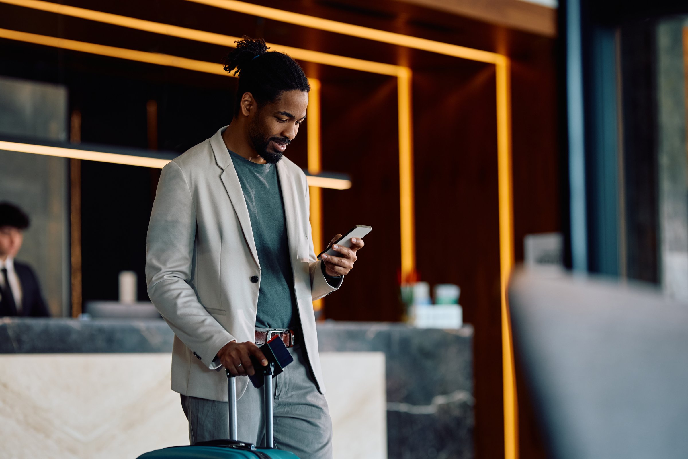 Happy African American man texting on mobile phone after checking in at the hotel. Copy space.