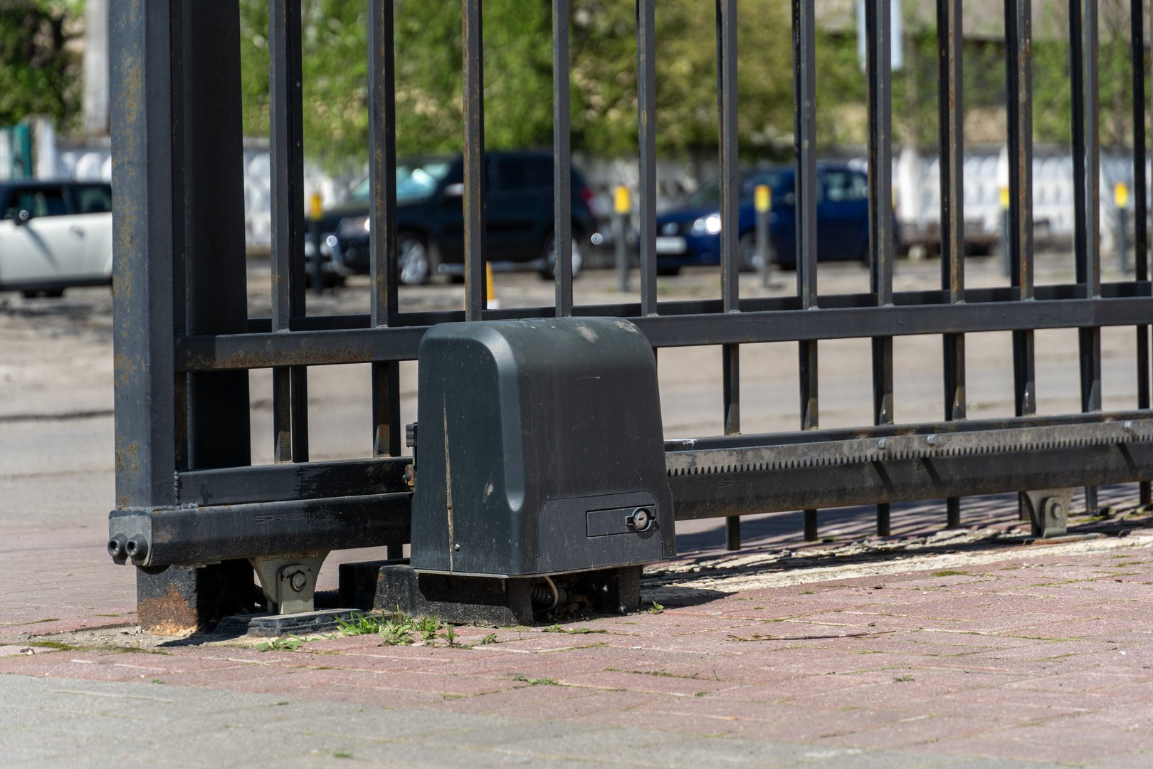 A motorized sliding gate made of black metal, featuring automation components on a brick surface, ensures property protection and secure access.