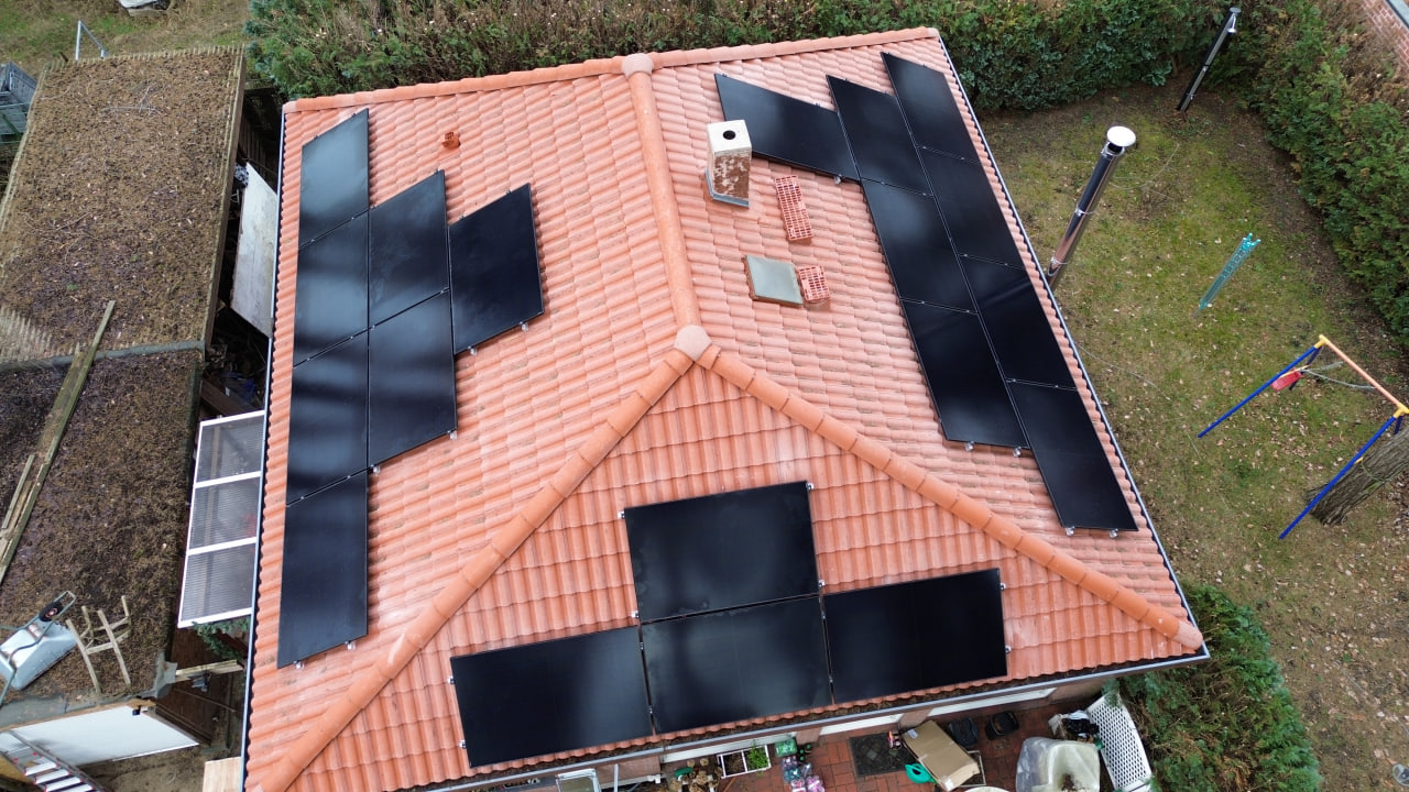 Aerial view of a red-tiled roof with multiple solar panels installed, surrounded by a garden and outdoor structures.
