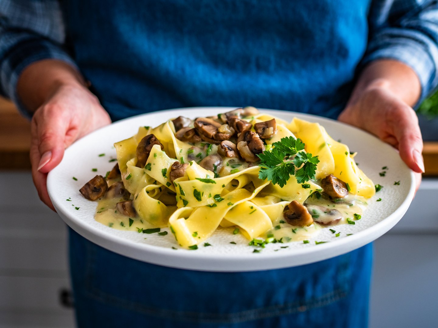 Woman holding plate with papperdelle pasta with champignons mushrooms in cream sauce and parsley