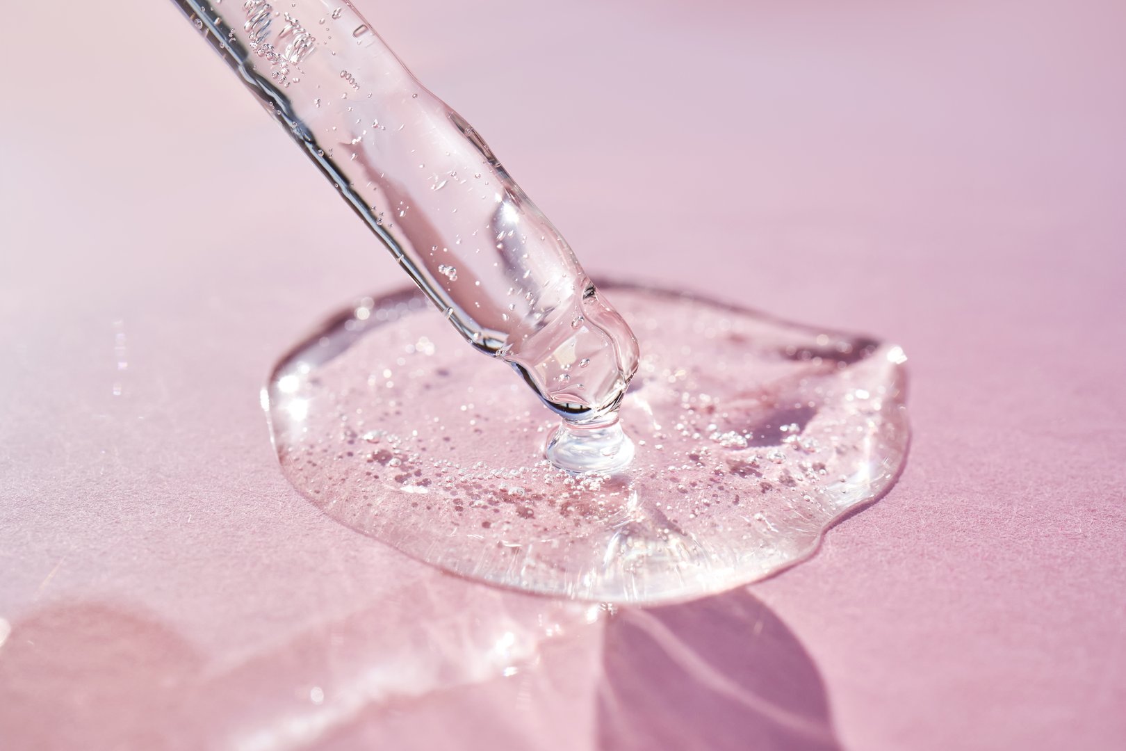 Pipette with serum shimmering in the sun on a pink background. High quality photo.