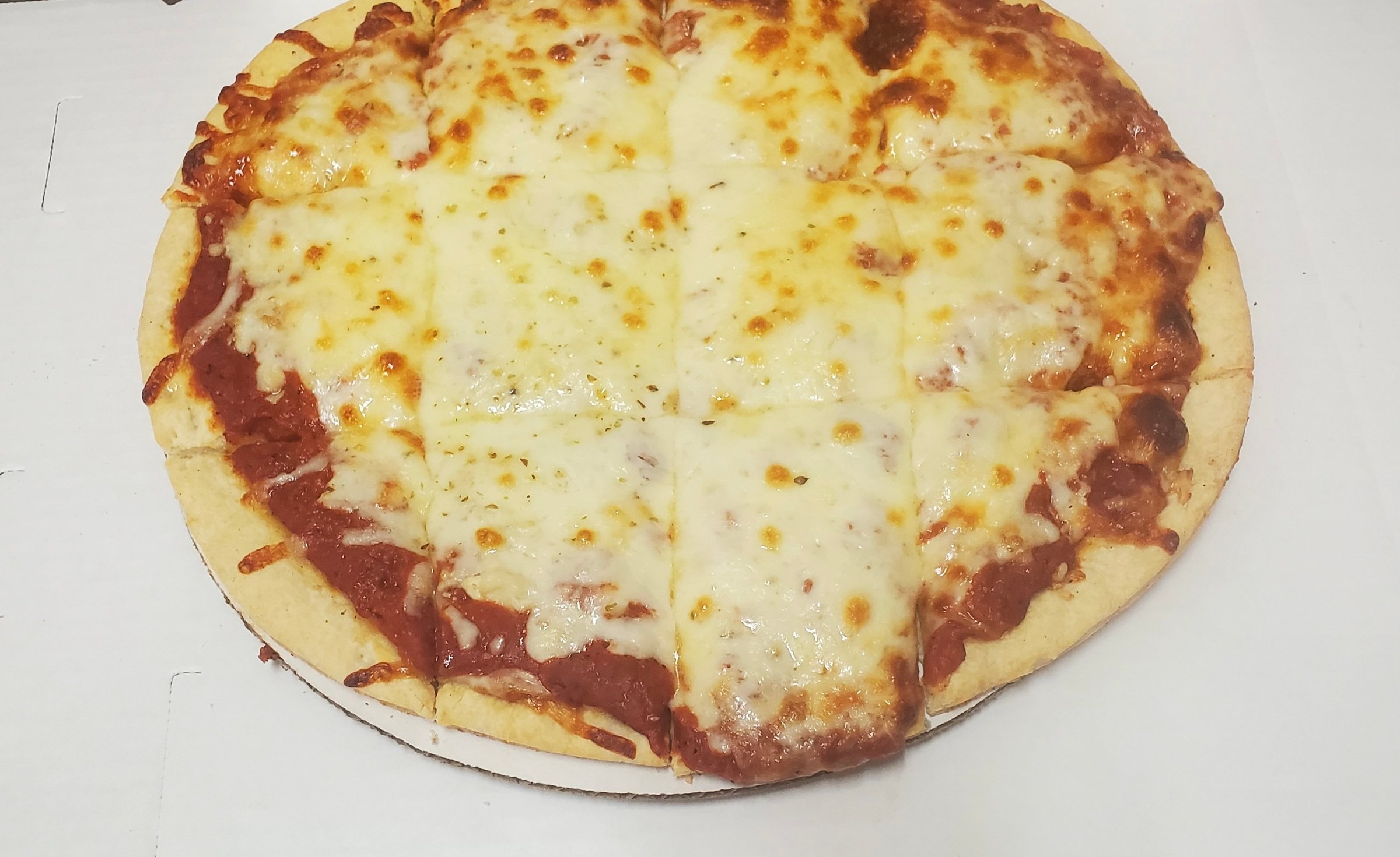 Cheese pizza with evenly melted cheese, cut into square slices, on a thin crust, displayed on a white surface.