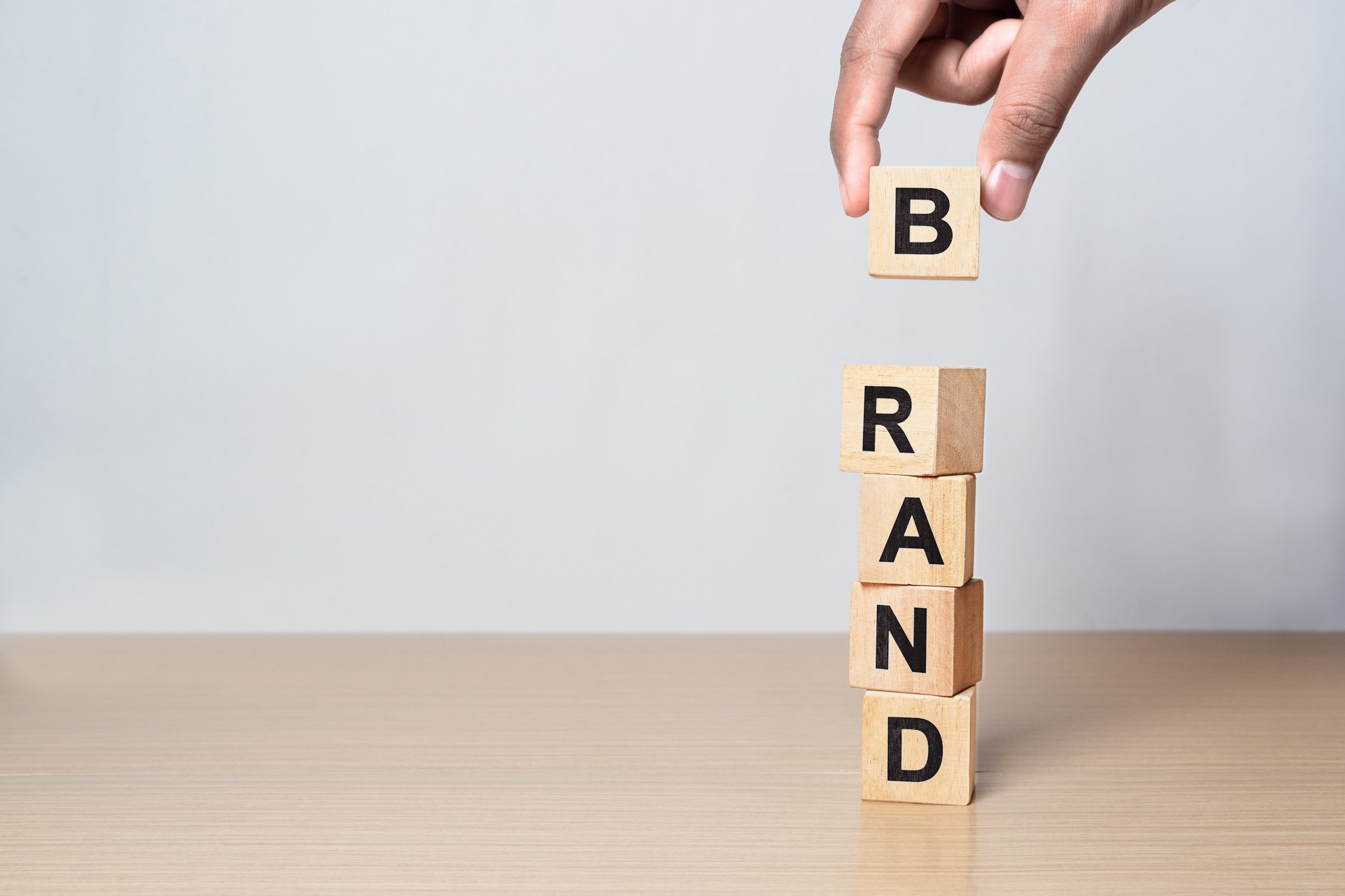 Hand placing wooden blocks spelling BRAND on a desk. Illustration for marketing strategy, branding growth, and business development concept