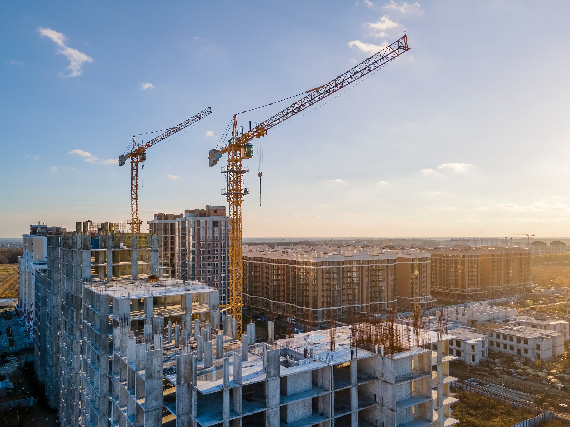 Cranes on the construction site surrounded by new real estates. Scenic aerial photo of growing city districts