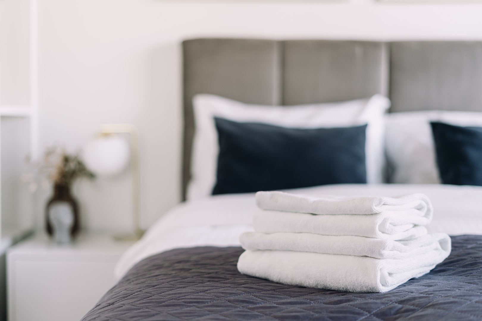 White towels on bed in hotel room. A well designed bedroom features a cozy bedding, linens and decorative cushions and pillows, creating an inviting atmosphere for a restful stay