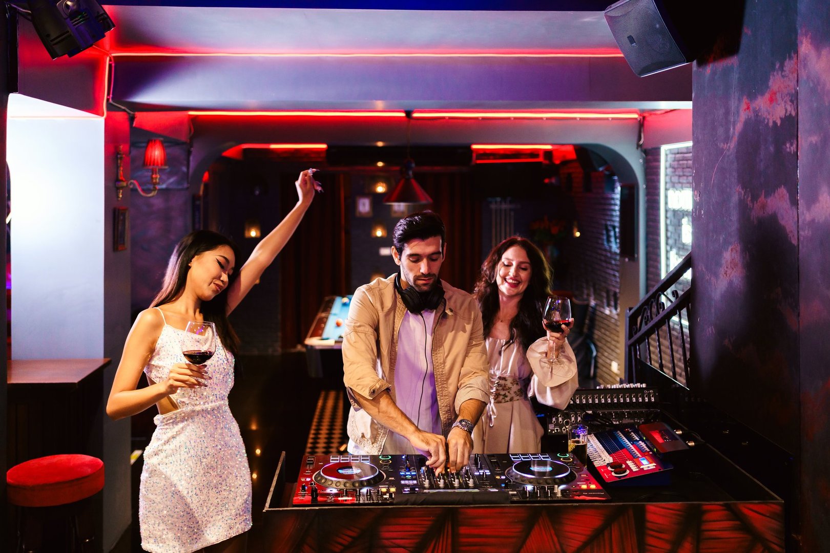Group of energetic women dancing friends with DJ enjoying night party. Young women dance in the nightclub. Nightlife, disco dance and girl's night party concept. Fun music festival