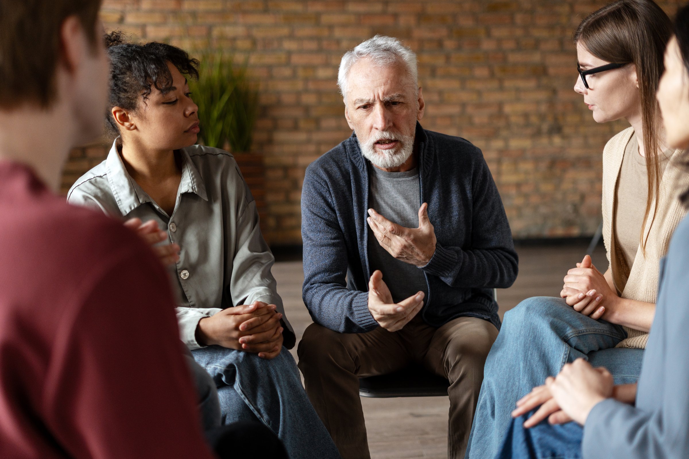 Diverse group of individuals engaged in listening to a senior man sharing insights during a supportive group therapy session
