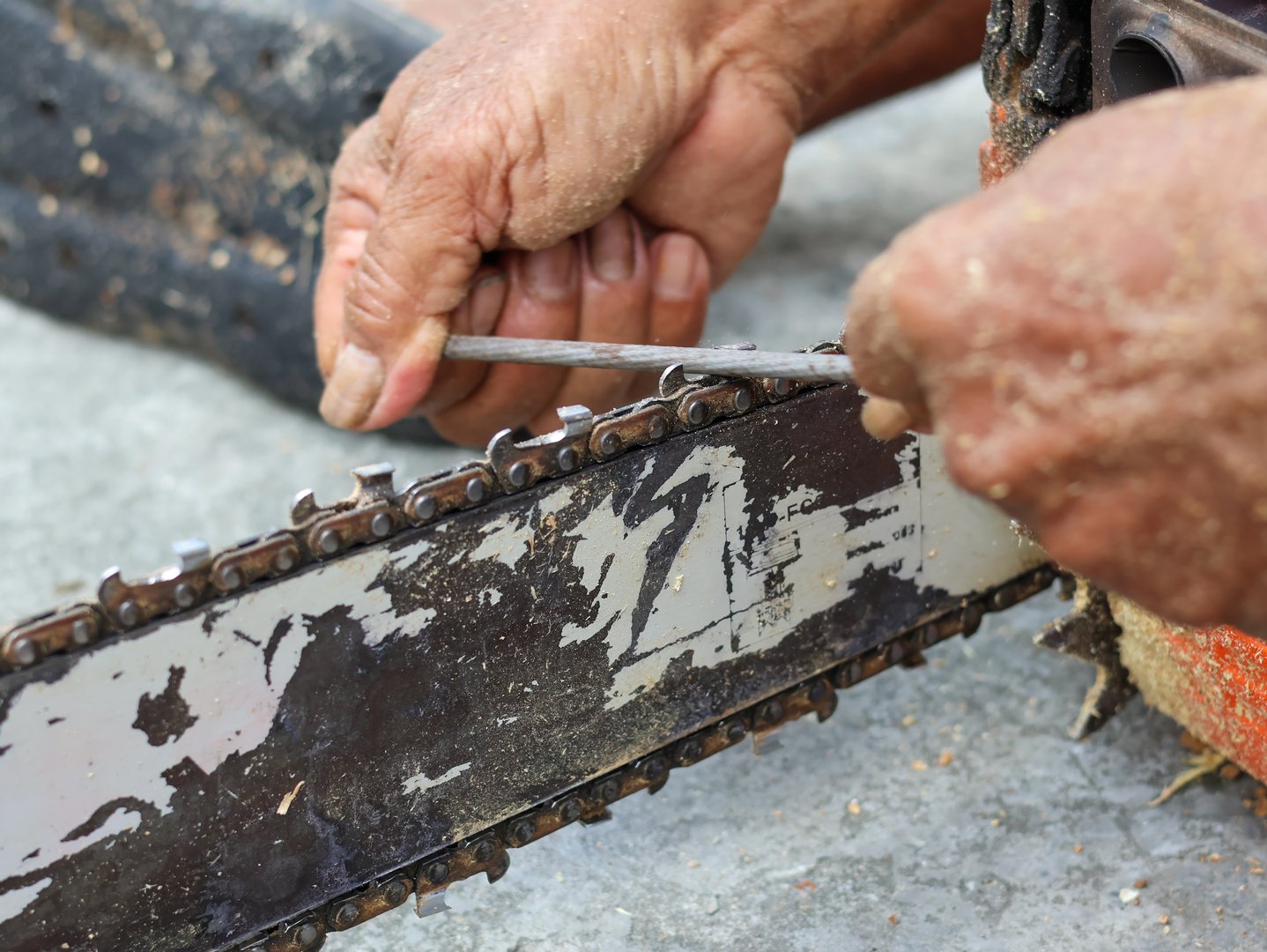 A worker's hands meticulously sharpen the chain of a chainsaw with a file, emphasizing maintenance, precision, and tool care.