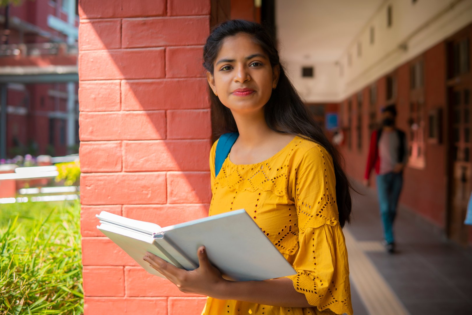 Portrait of beautiful Asia, Indian female college student standing in campus corridor with books and looking at the camera with a toothy smile