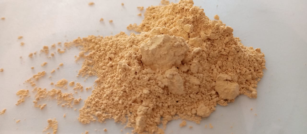 A pile of light brown powder on a smooth white surface, showing fine and coarse granules.