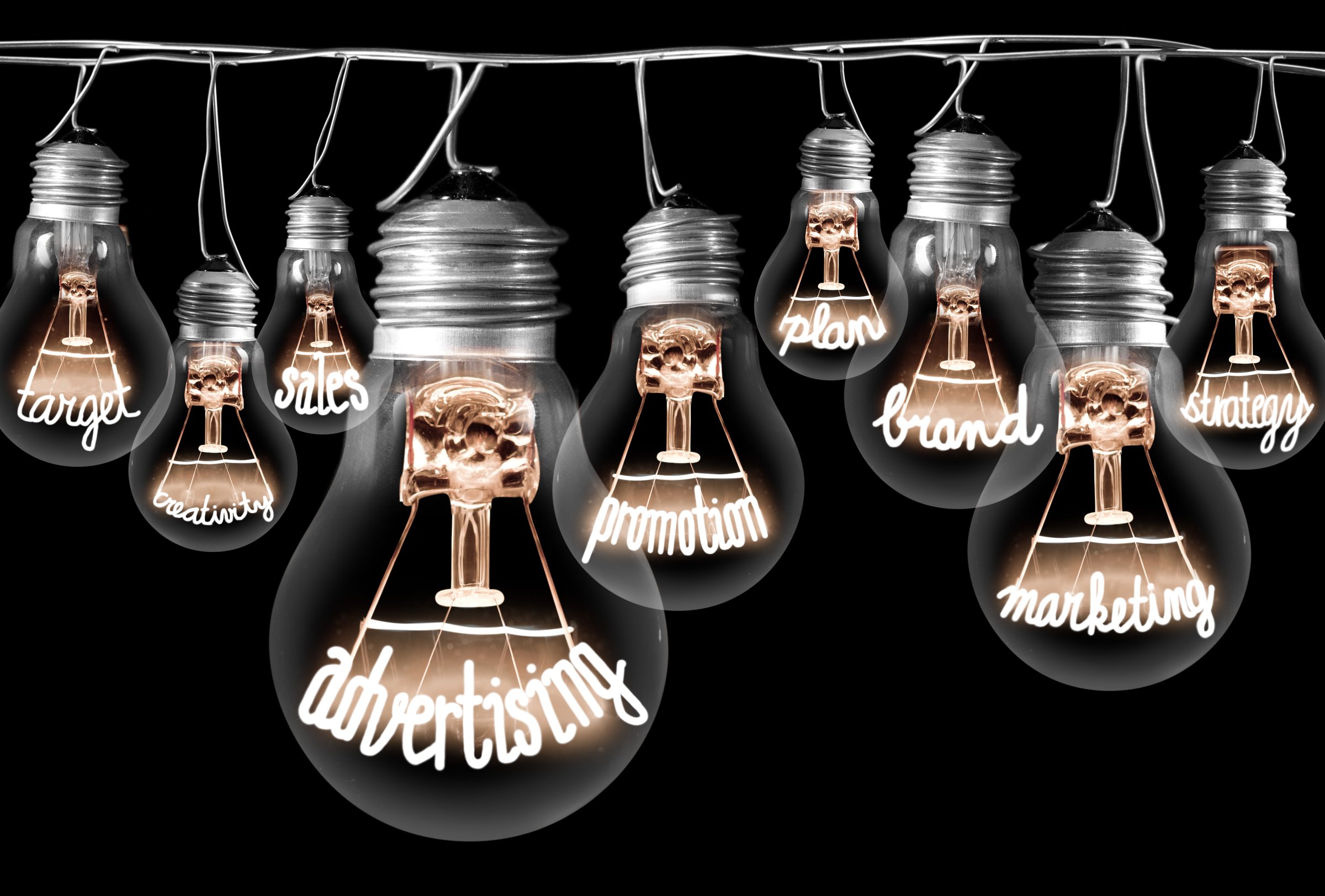 Photo of light bulbs with shining fibres in shapes of ADVERTISING concept related words isolated on black background