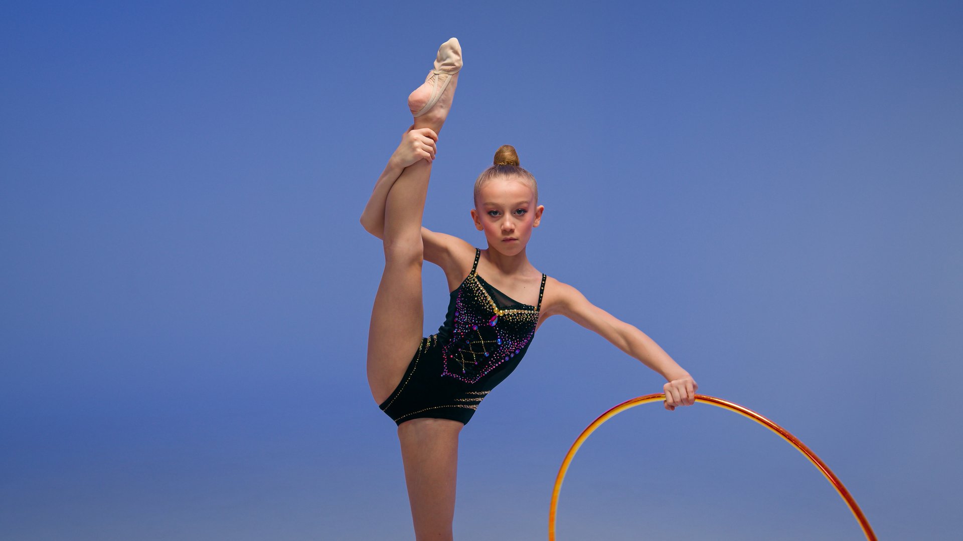 Caucasian little girl child kid daughter schoolgirl gymnast athlete dancer ballerina acrobat stand in split position flexibility artistic gymnastics spinning hoop sport event studio blue background. High quality 4k footage