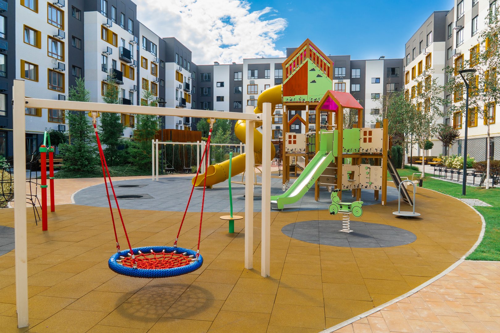 Colorful children's playground with rubber coating, swings, slides, and other equipment in a residential area