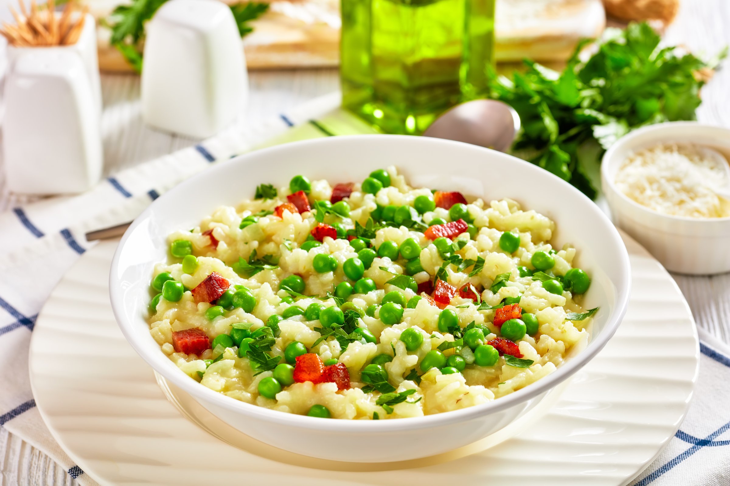 Risi e Bisi, Venetian Risotto with Spring Peas and chunks of ham in a bowl on a white table with ingredients, italian cuisine, horizontal view from above, close-up