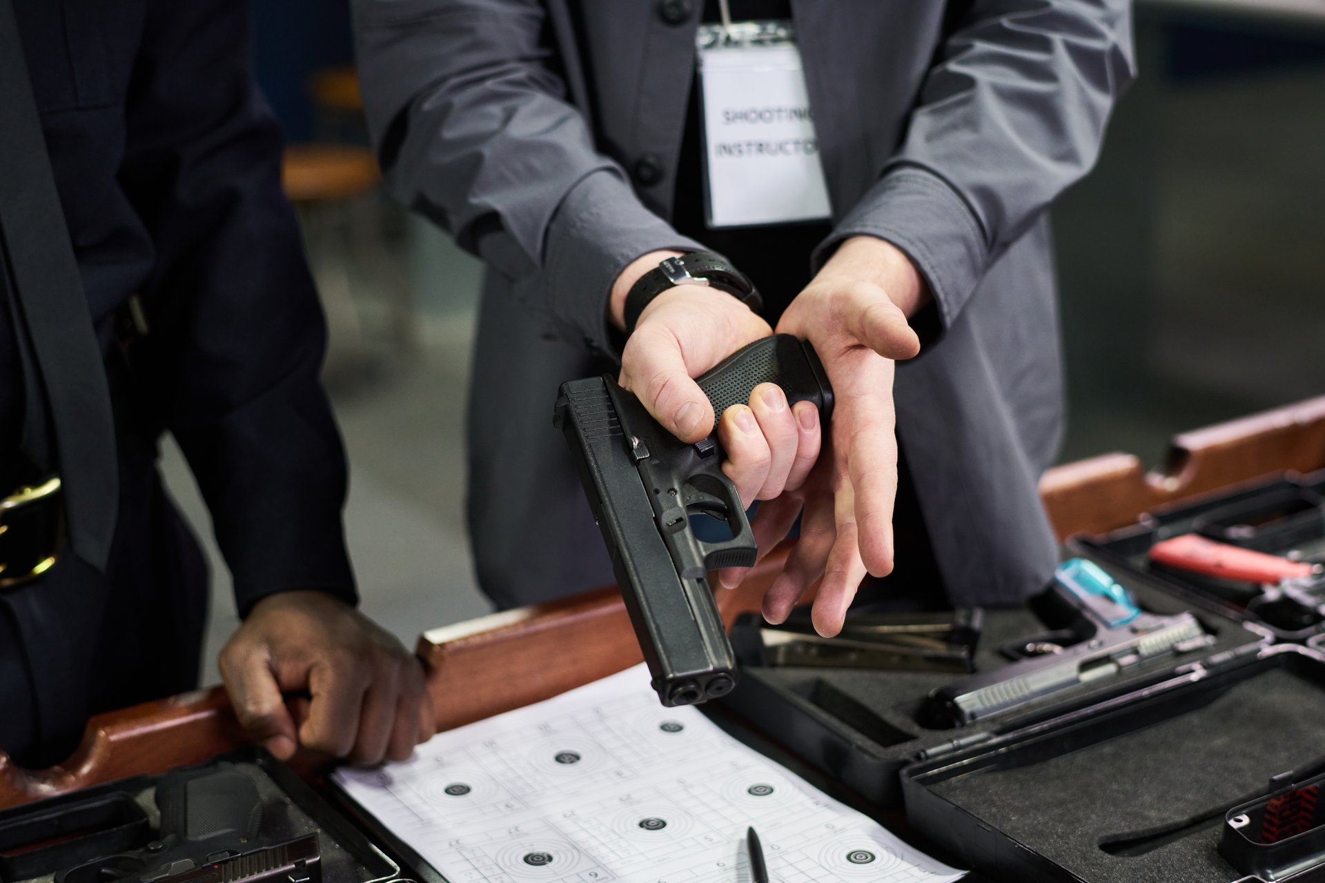 Close-up shot showing instructor guiding individual on proper handgun handling technique during firearm safety training in an indoor range environment