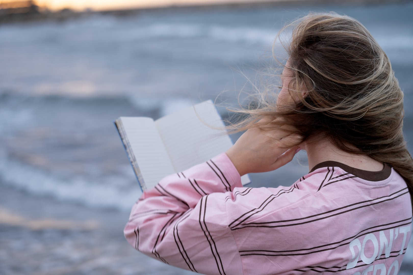 Woman reading notebook outdoors, wind blowing hair by the ocean
