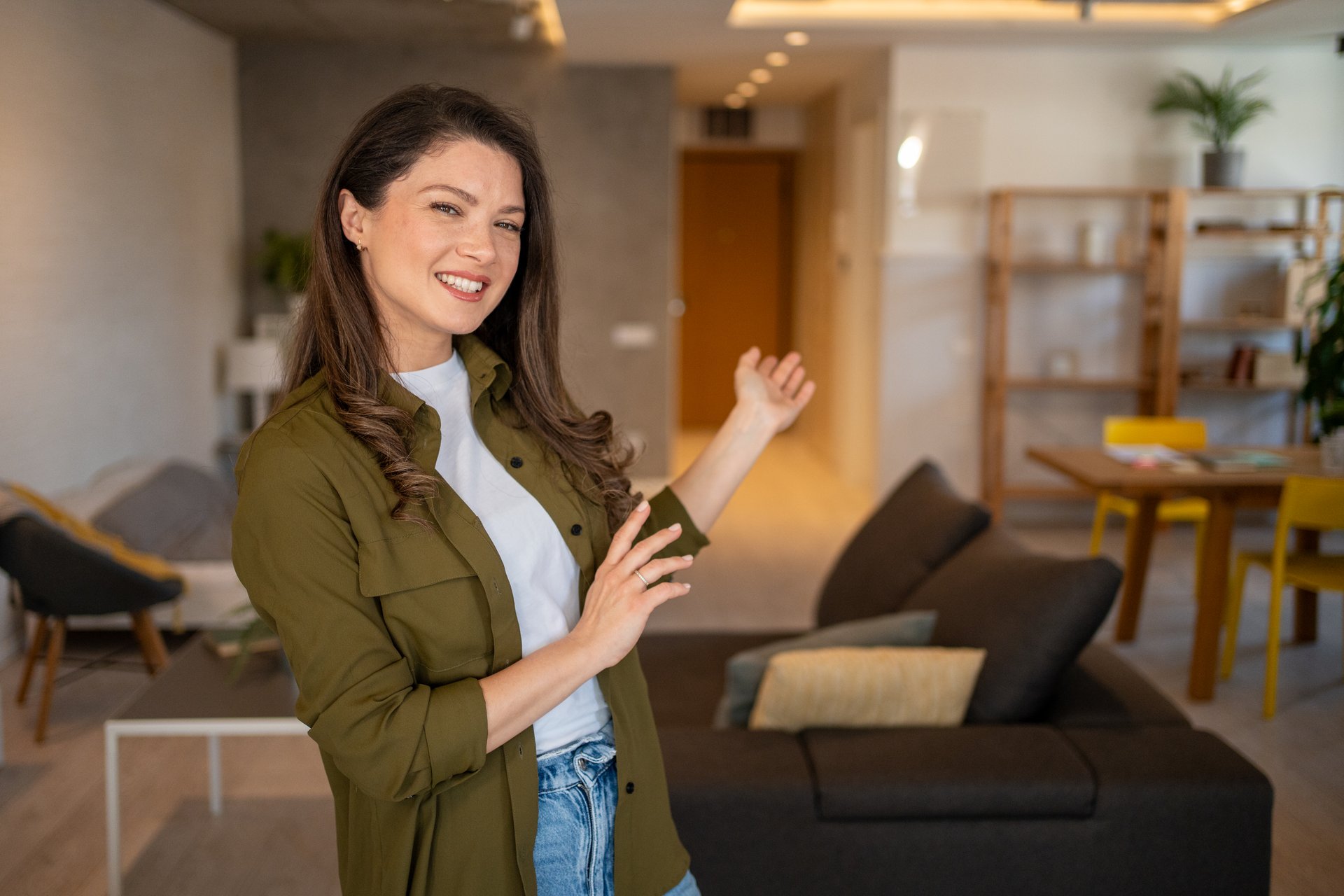 Cheerful female real estate agent presenting a furnished apartment to potential buyers, highlighting its modern design and amenities with a welcoming smile