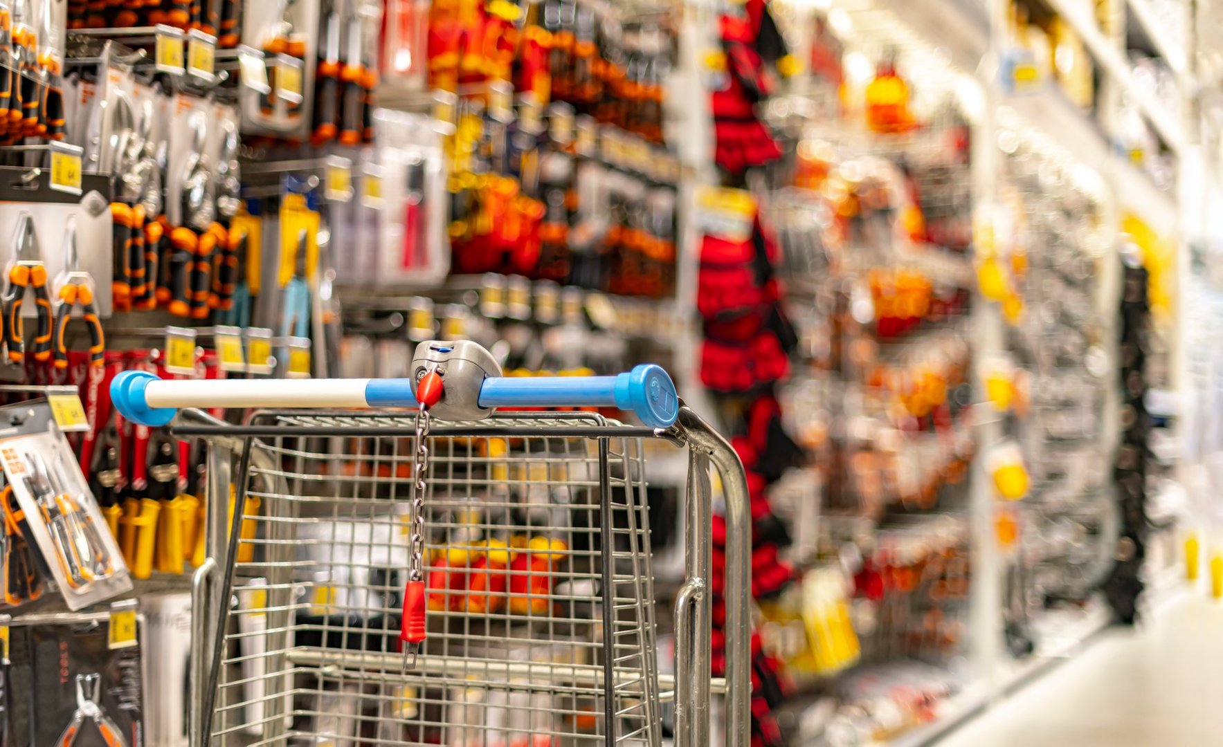 A shopping cart by a store shelf in a hardware store.