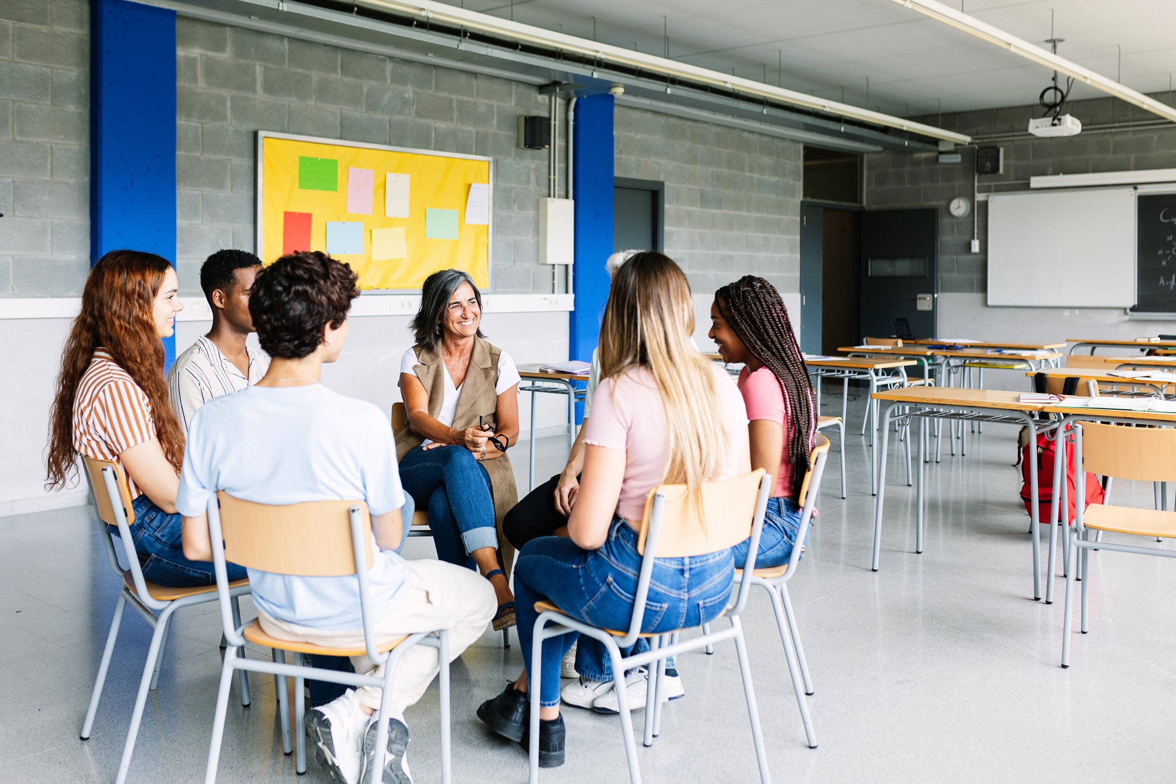Young group of teenage students discussing in classroom sitting in circle with female teacher, giving an opinion on a debate topic. Education concept