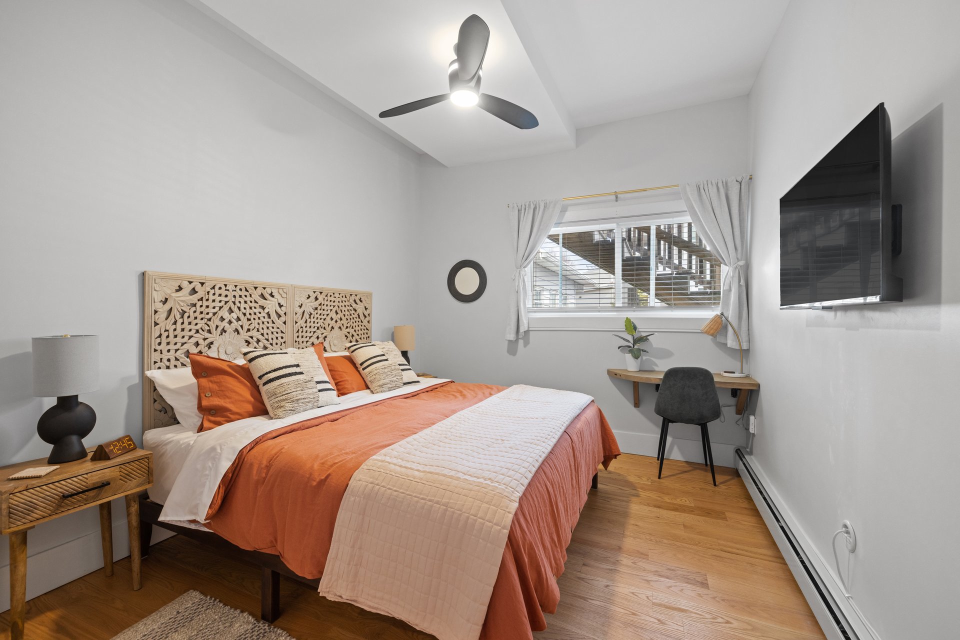 A cozy bedroom with a TV, windows, and hardwood floors