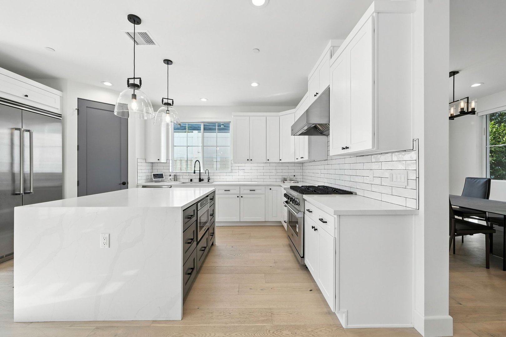 Modern kitchen interior with white cabinetry, large island, stainless steel appliances, and pendant lighting