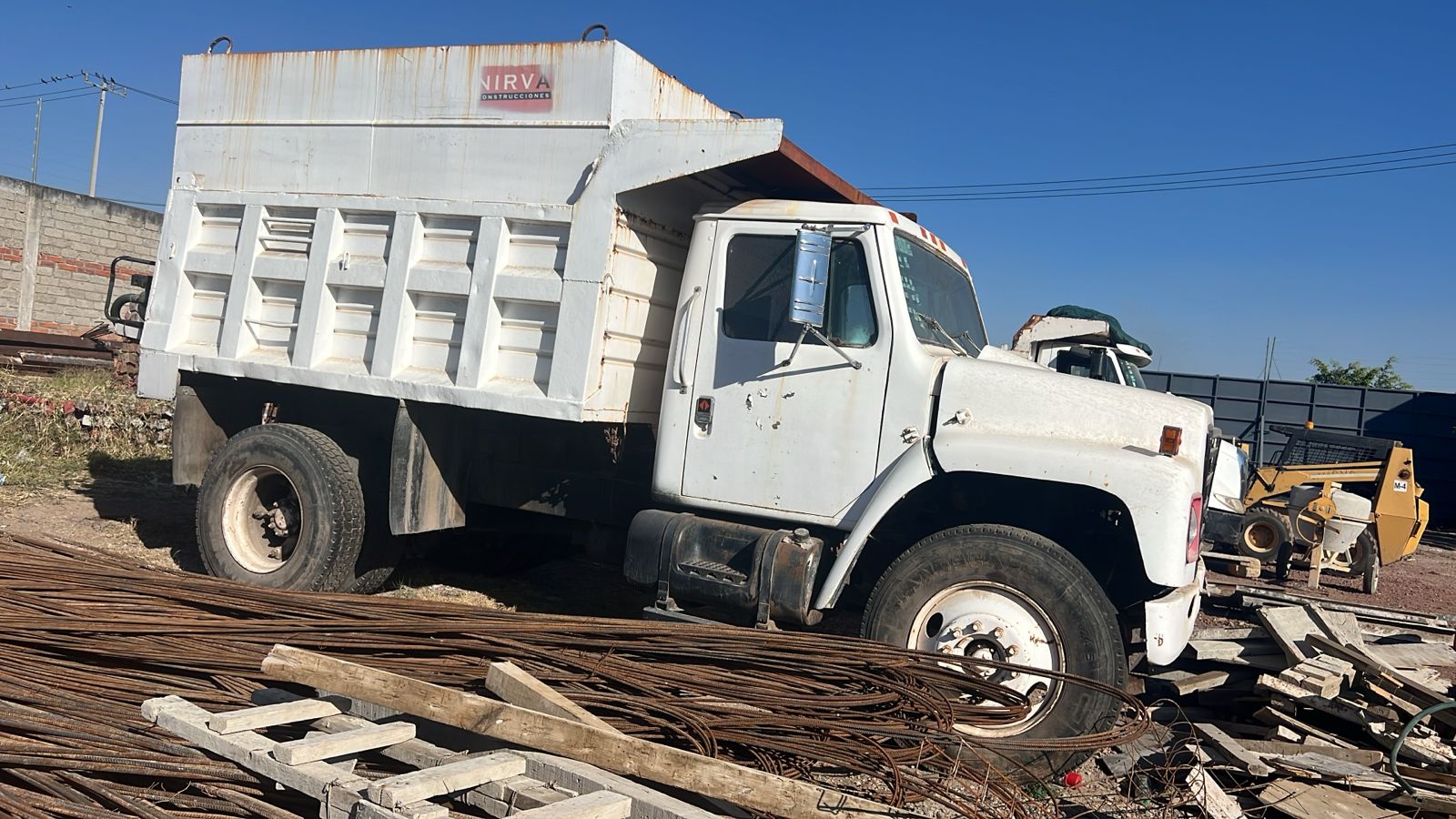 A white dump truck parked in a scrapyard with metal debris and construction materials around it.