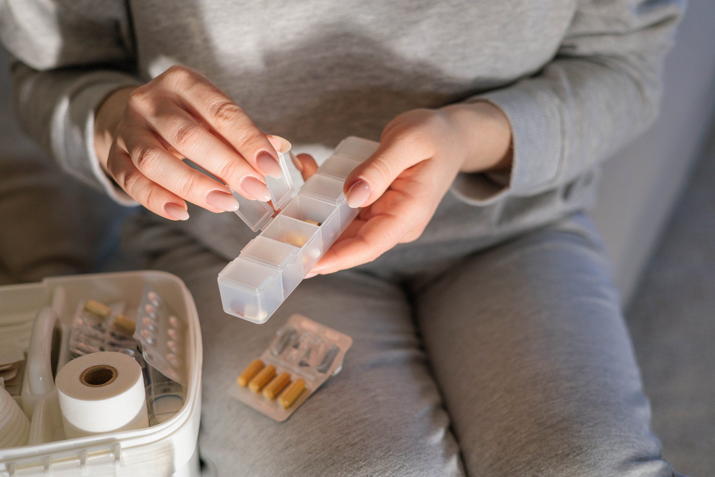 Closeup female hand neatly placing medicament at domestic first aid kit top view. Storage organization in transparent plastic box drug, pill, syringe, bandage. Fast health help safety emergency supply