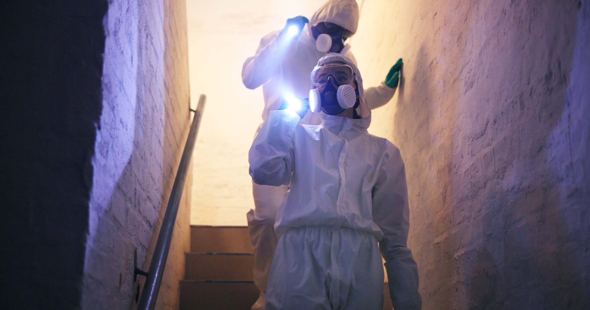 Hazmat, suit and people for disinfection walking with flashlight on stairs in basement for toxic spill or biohazard chemical inspection. Dark underground, forensic investigation or team with gas mask