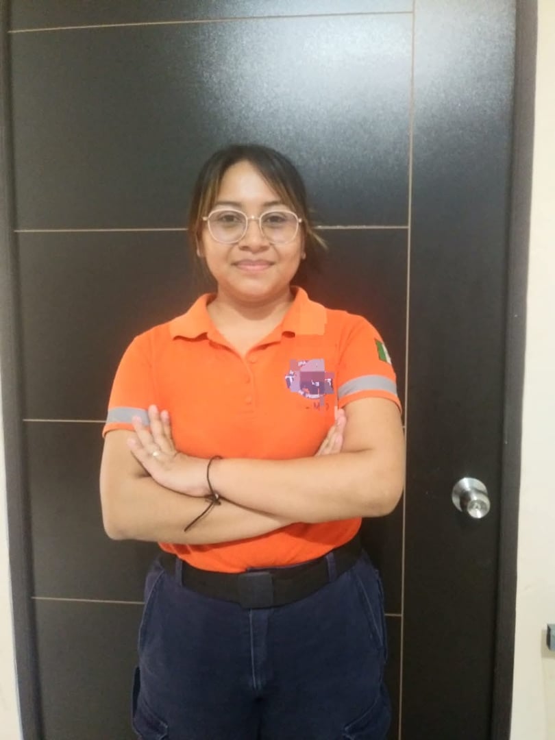 A person wearing an orange shirt and glasses stands with arms crossed in front of a dark door.