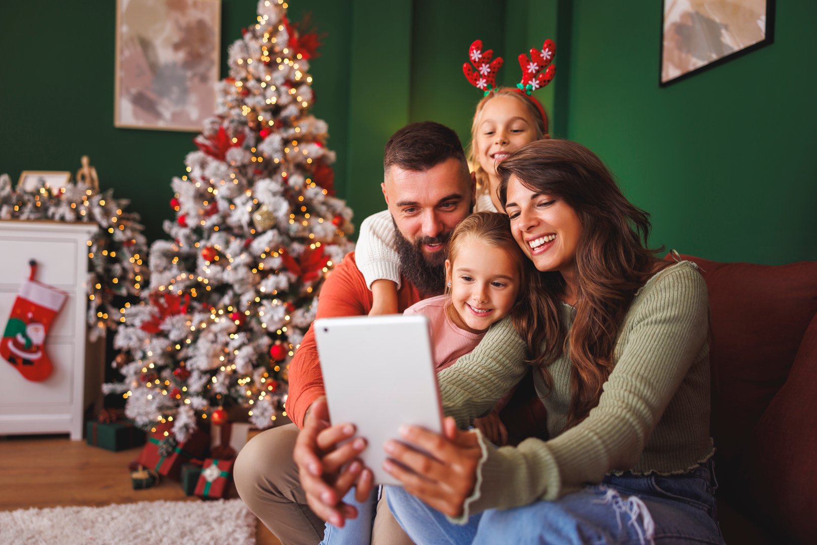 Beautiful happy young family having fun taking selfies by the Christmas tree using tablet computer while spending Christmas day together at home