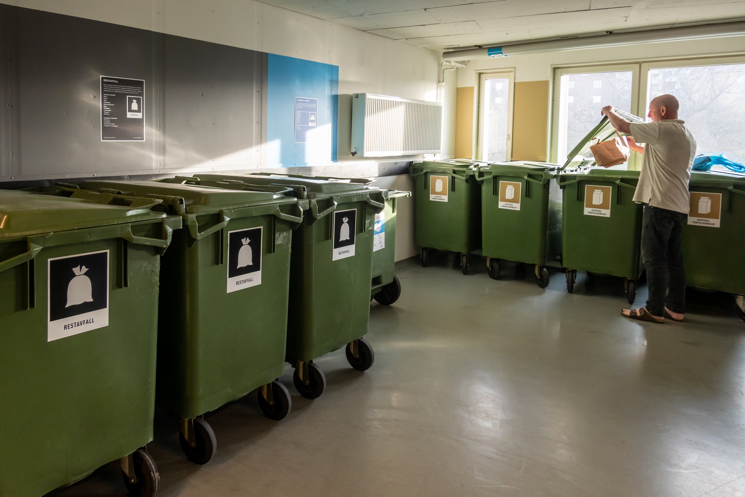 Stockholm, Sweden A man throws garbage in a super clean and organised garbage room in a residential housing complex.The labels denote type of waste in Swedish.