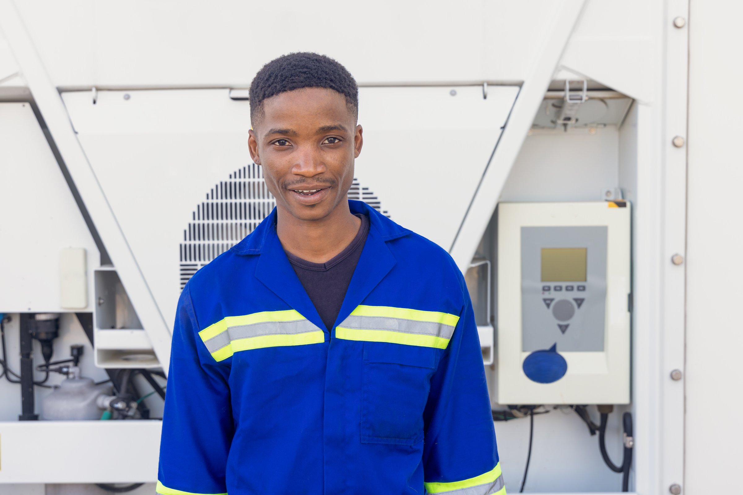 portrait of single african man worker industrial setting outdoors in front of a mobile air conditioner cooling unit,