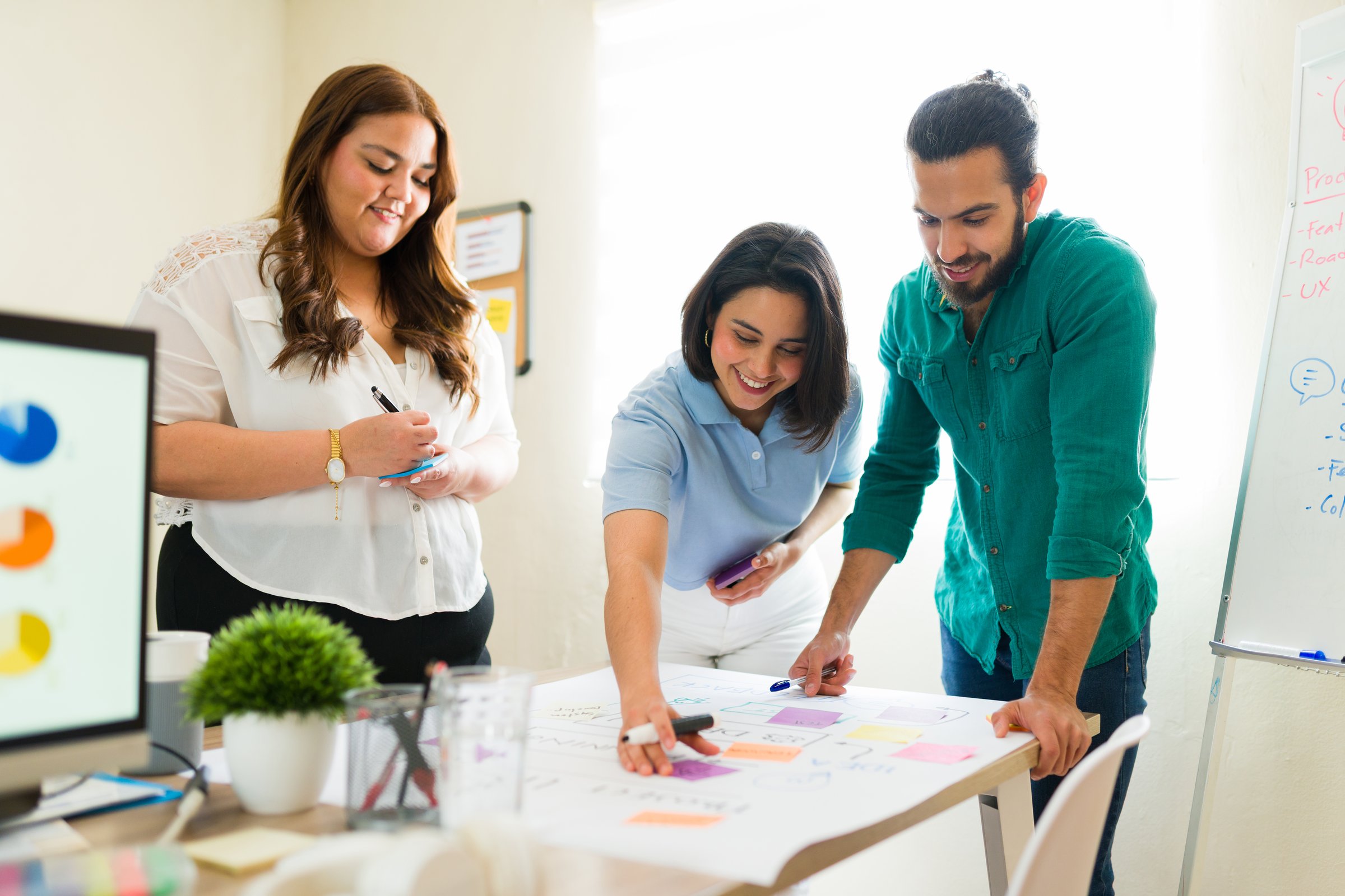 Latinx entrepreneurs working together on a project in modern office using colorful sticky notes during a productive meeting