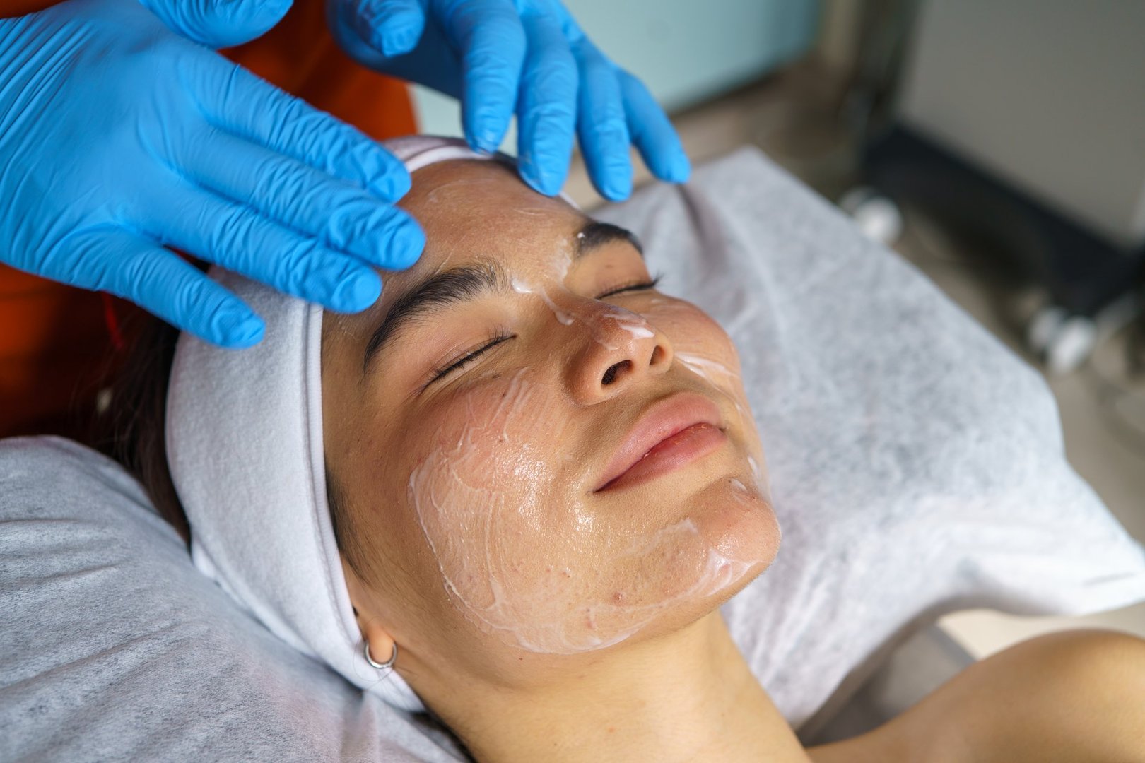 Young adult receiving a professional facial treatment with anti-acne cream applied. Aesthetician wearing gloves gently massages the face for skincare rejuvenation