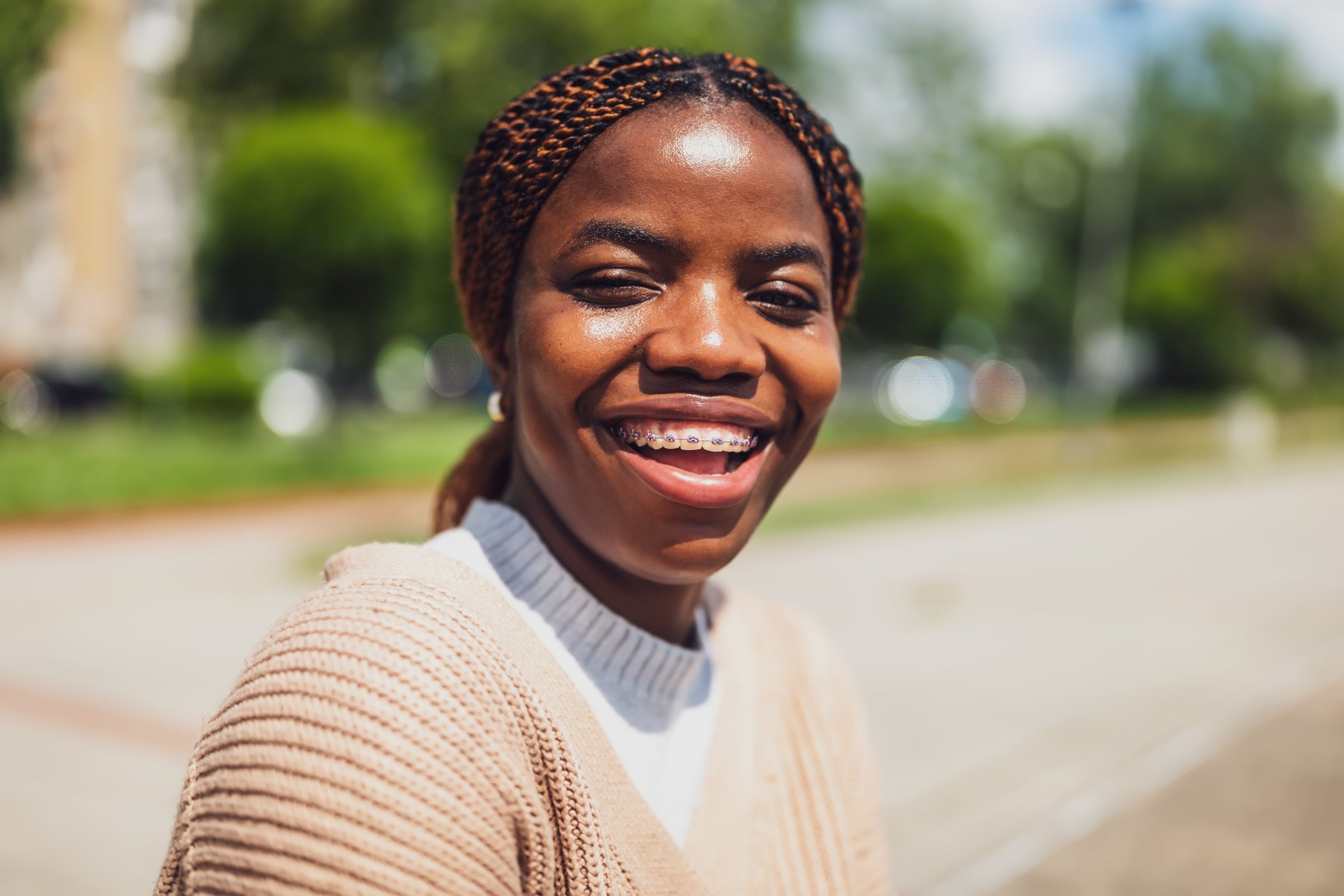Close up portrait of cheerful young African American woman with braces, smiling brightly on a sunny day.