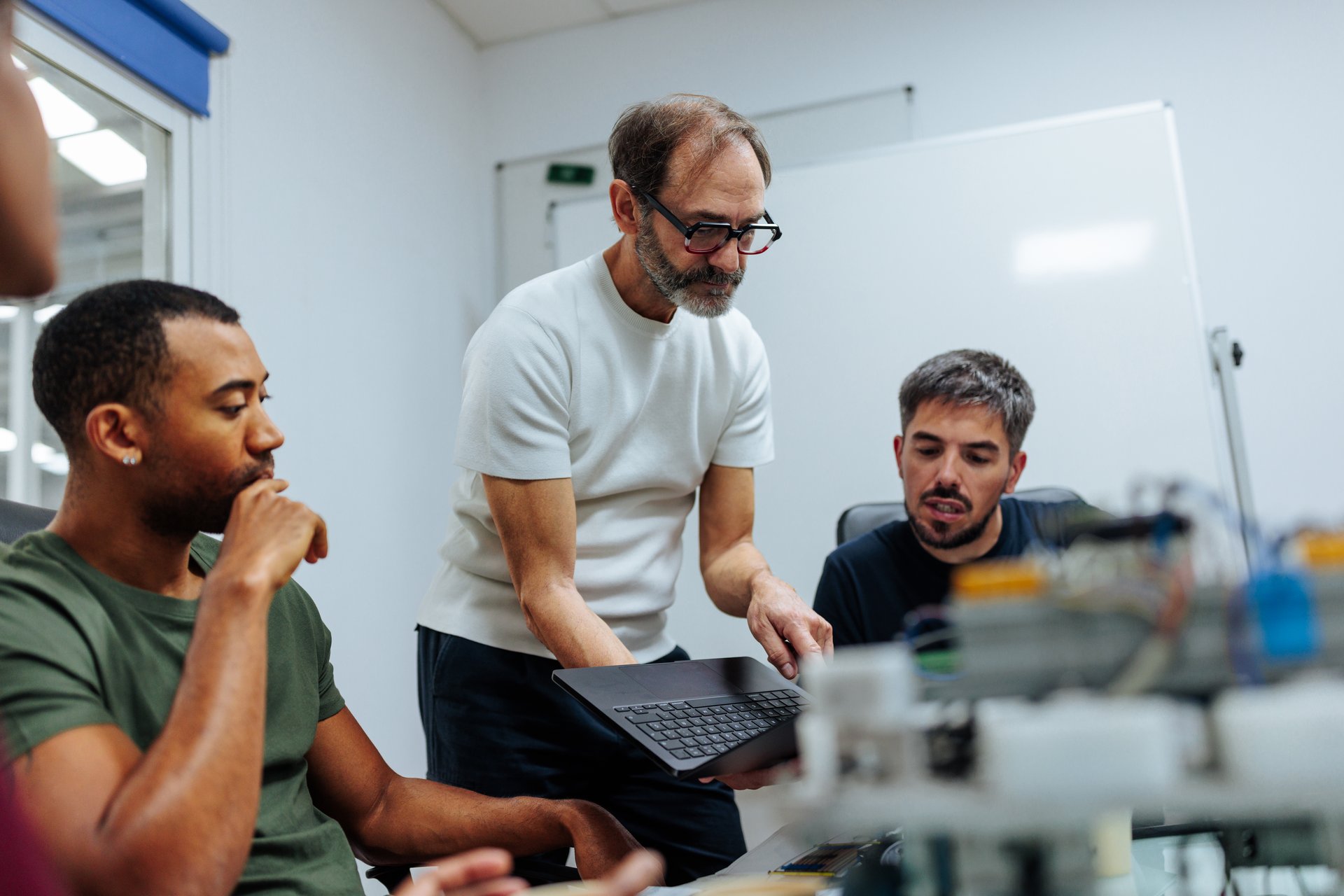 Engineering team working together, analyzing data on a laptop, developing and testing a complex robotic system in a modern laboratory