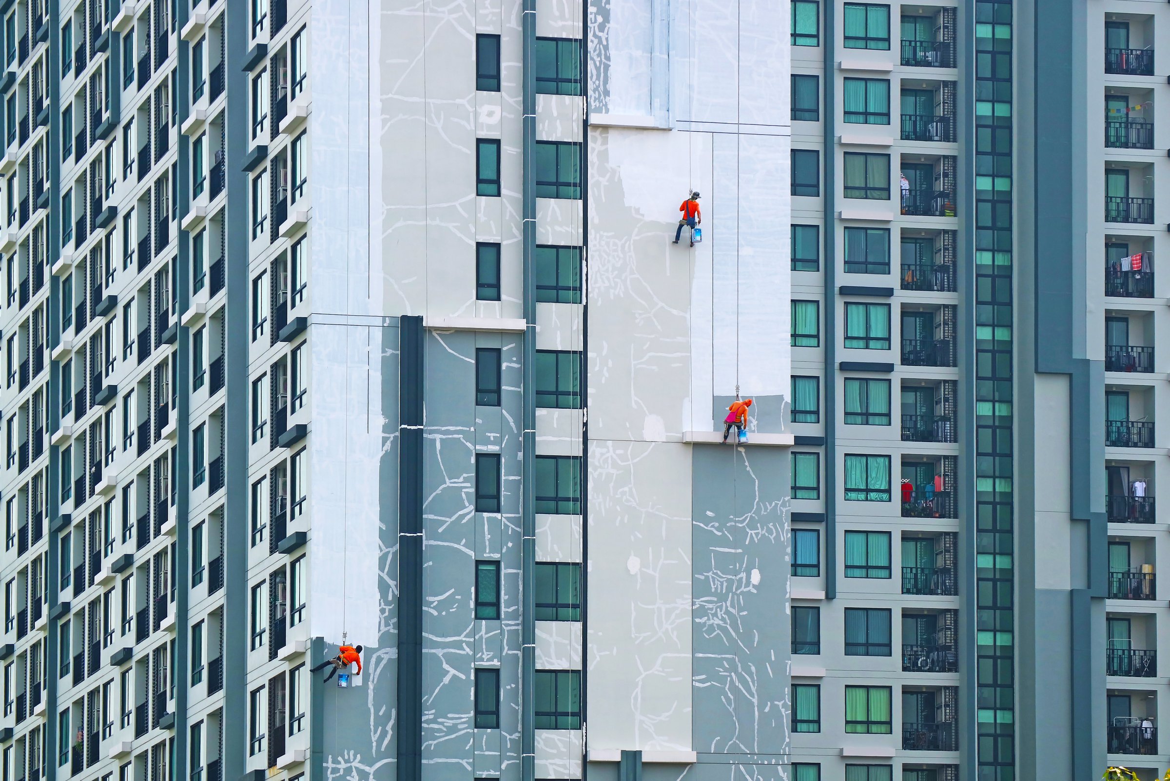 Three of rope access workers painting the facade of a high residential buildings