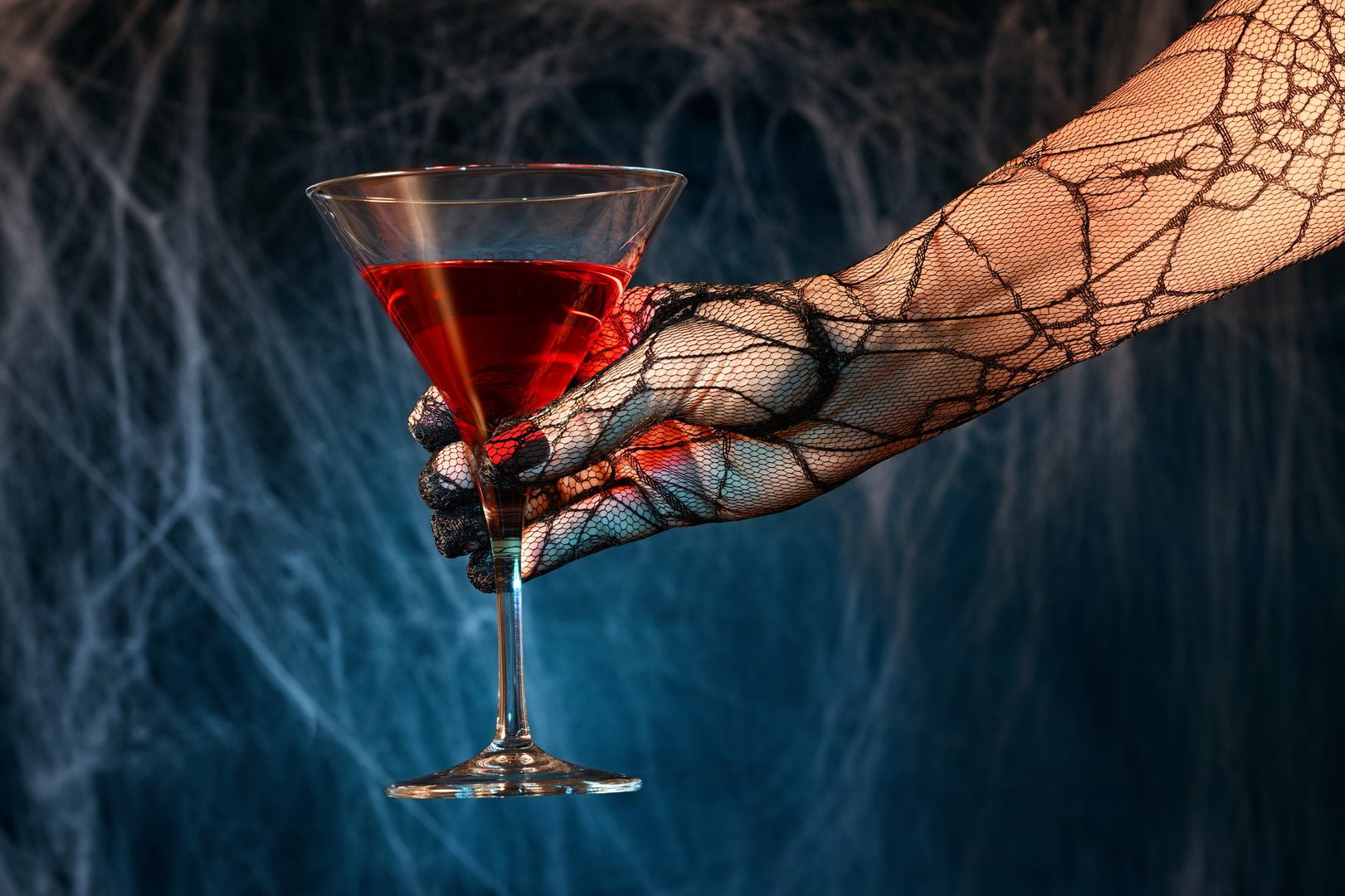 Gloved female hand with red cocktail on spiderweb background