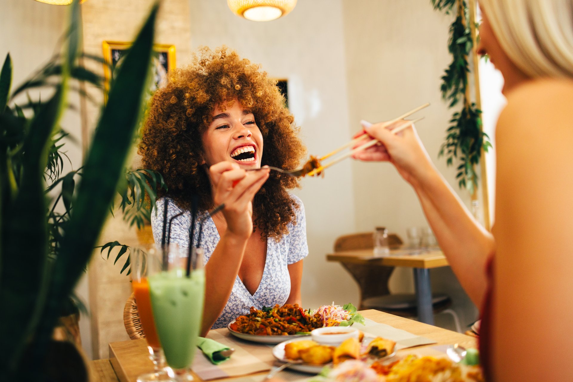 Two female friends are enjoying a meal together in a modern asian restaurant laughing and sharing food with chopsticks