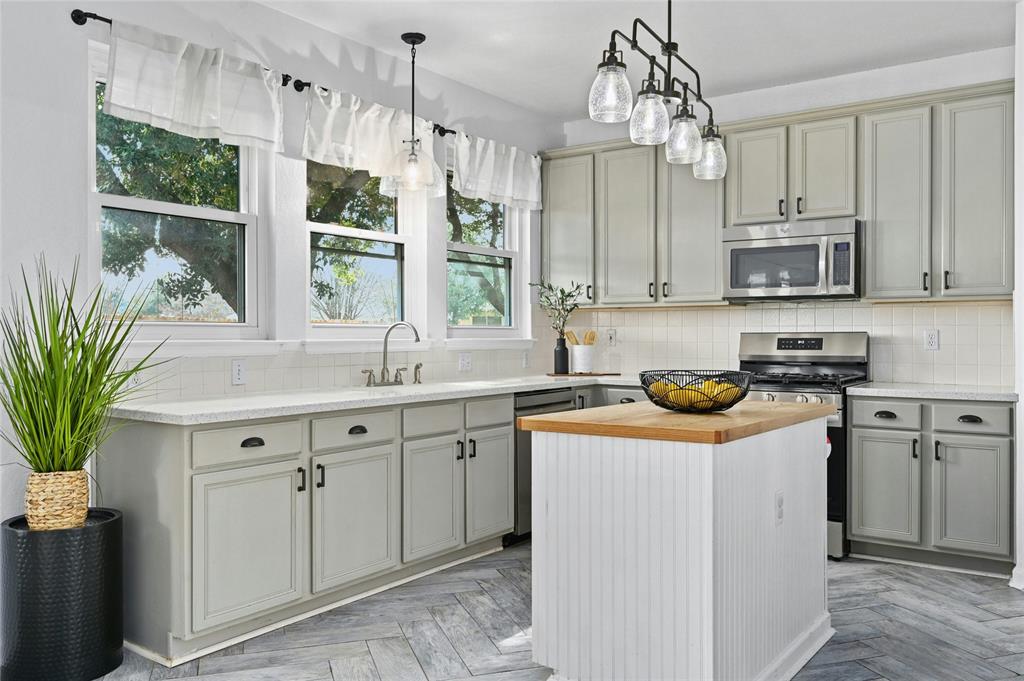 Modern kitchen with light gray cabinets, white countertops, stainless steel appliances, and a small island with wooden top.