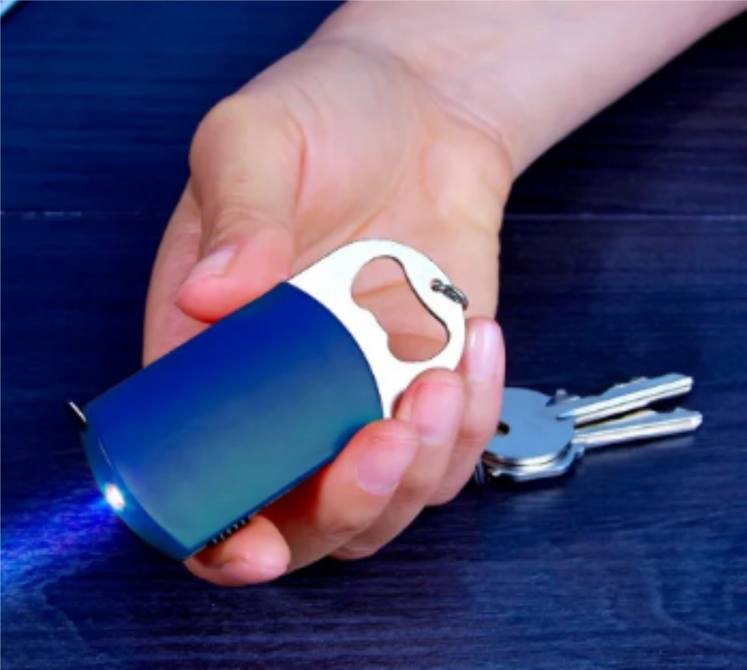 A hand holding a small blue emergency tool featuring a bottle opener and LED light, with keys on a keyring nearby.