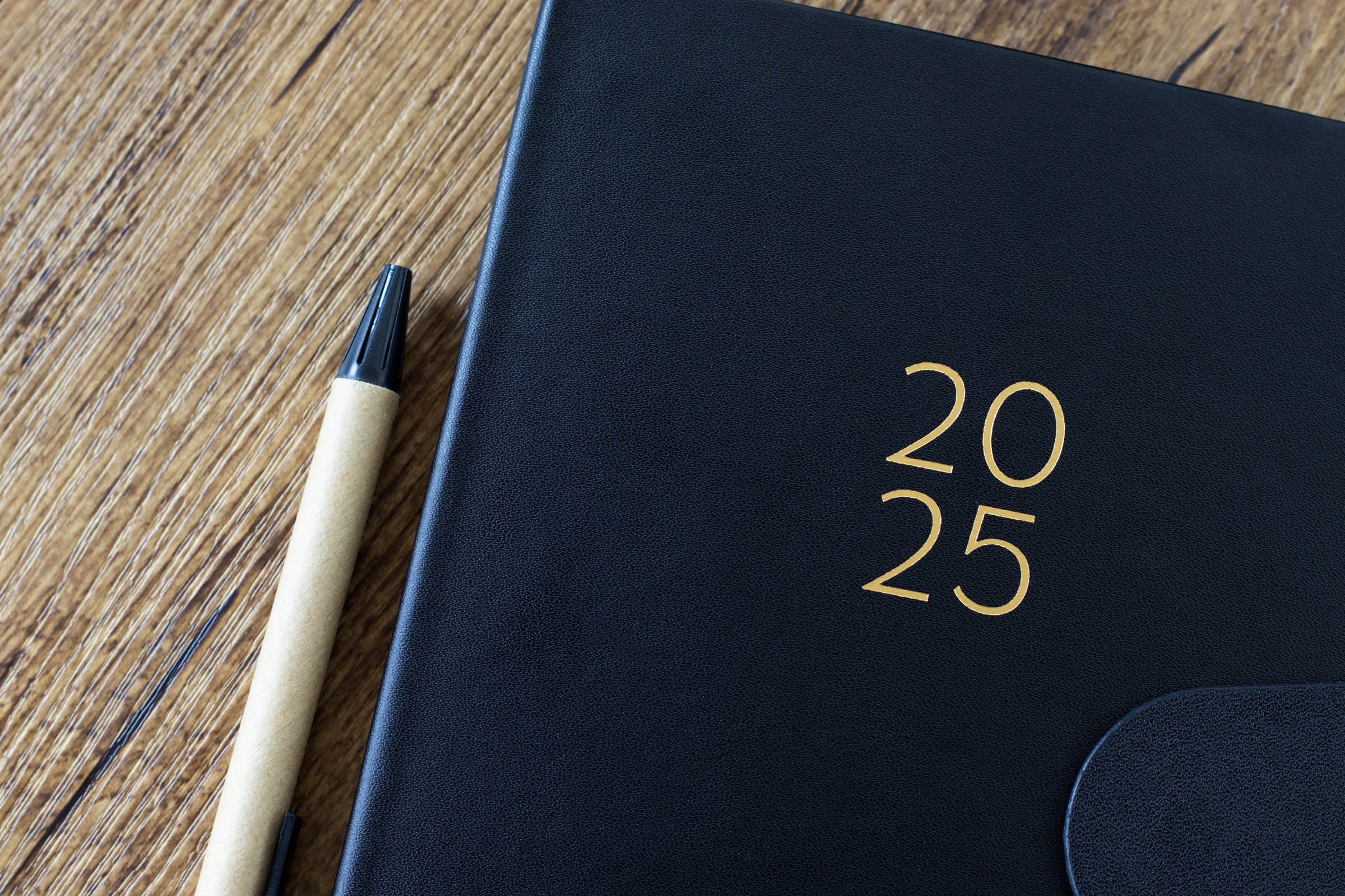2025 new year notebook with pen on wooden desk. Top view. Calendar planner, annual organizer, business event schedule concept.