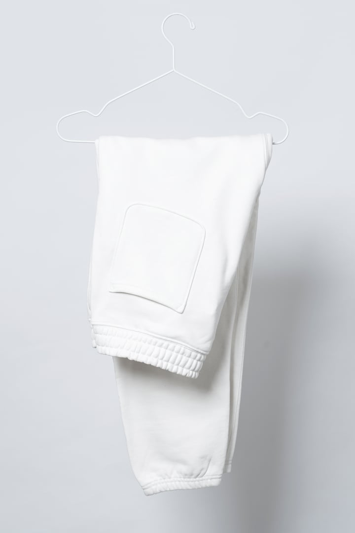 Blank white sweatpants hanging on the thin metallic hanger against light gray background