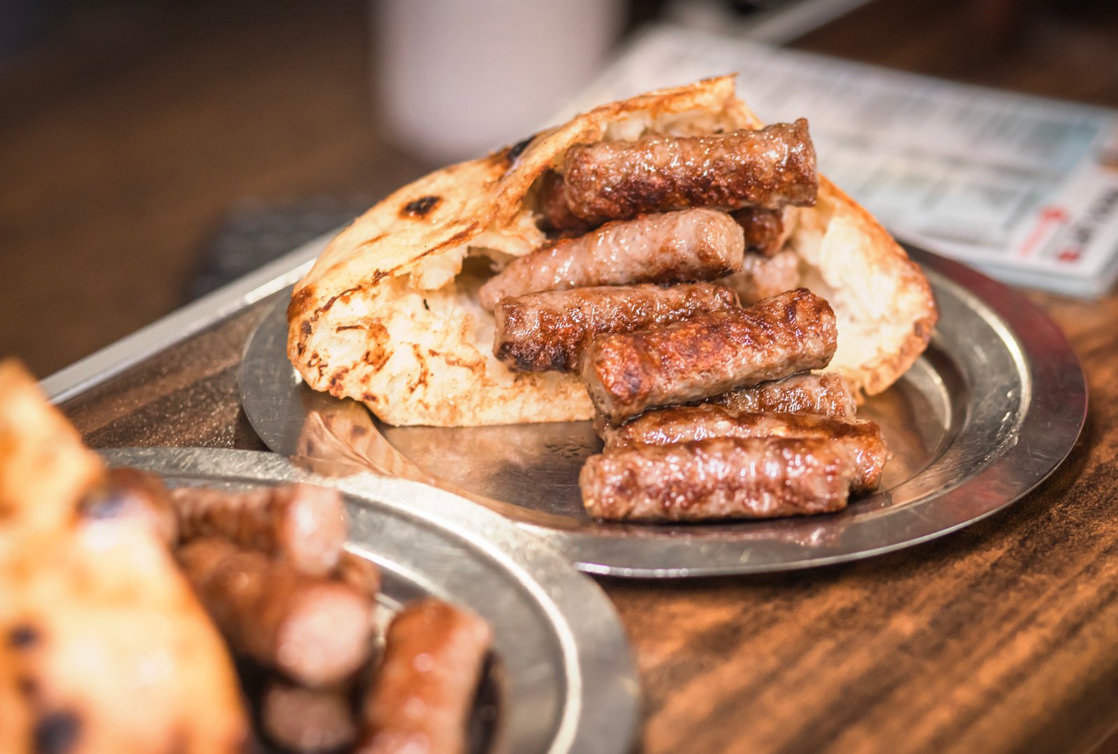 Close-up of delicious Balkan grilled cevapcici served with warm flatbread on a rustic metal plate. Perfect for conveying traditional cuisine, food culture, and culinary travel experiences.