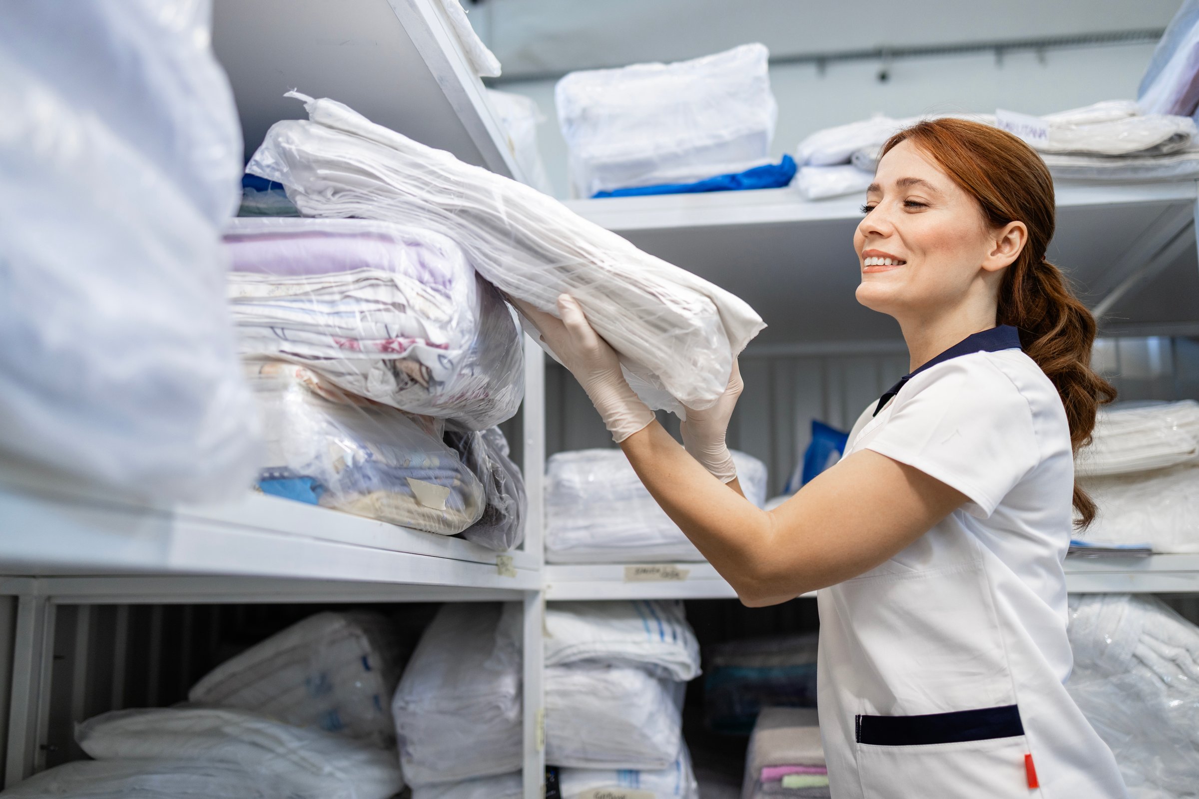 Beautiful caucasian worker stacking clean laundry on the shelf.