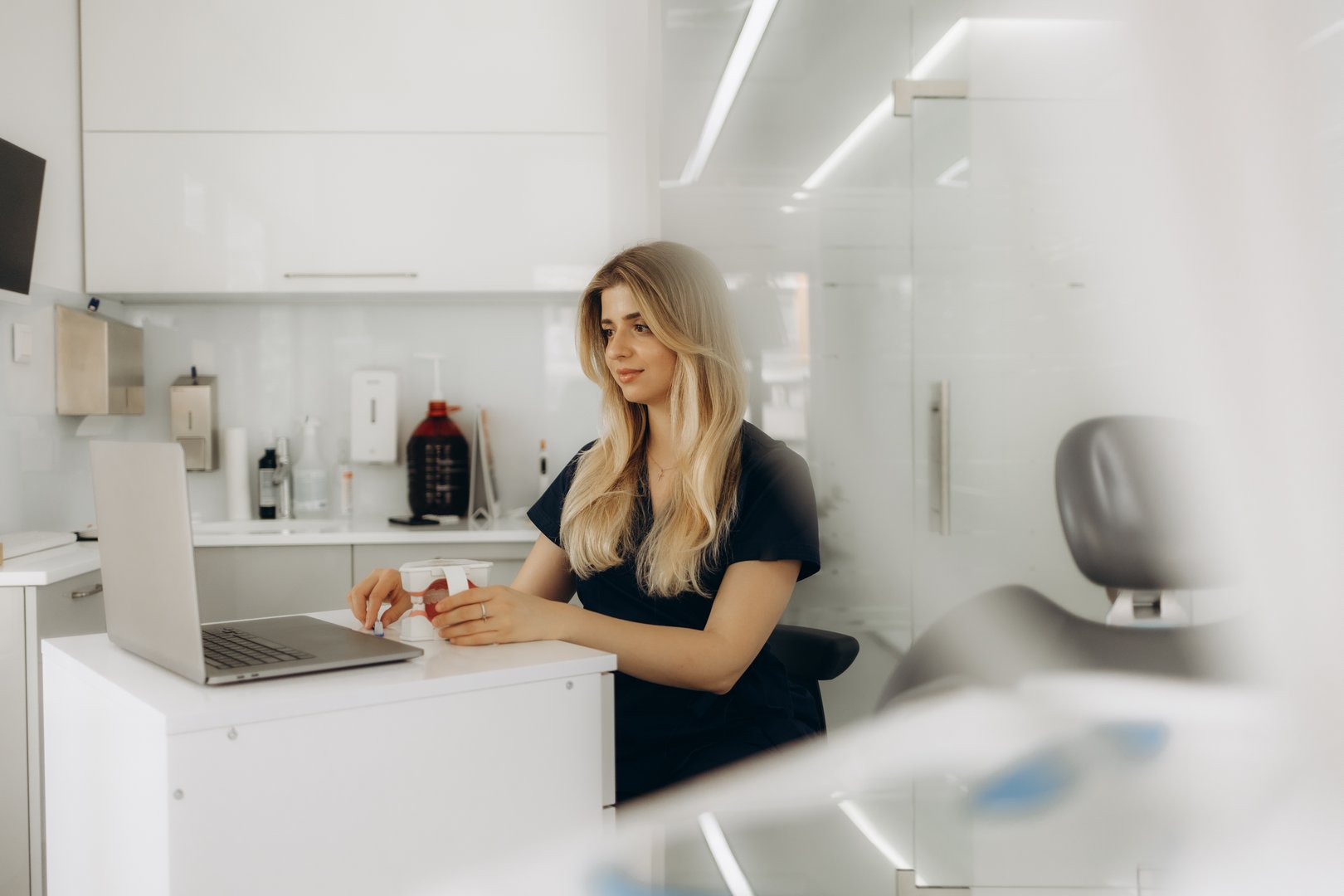 Pensive female dentist writing on laptop in her office