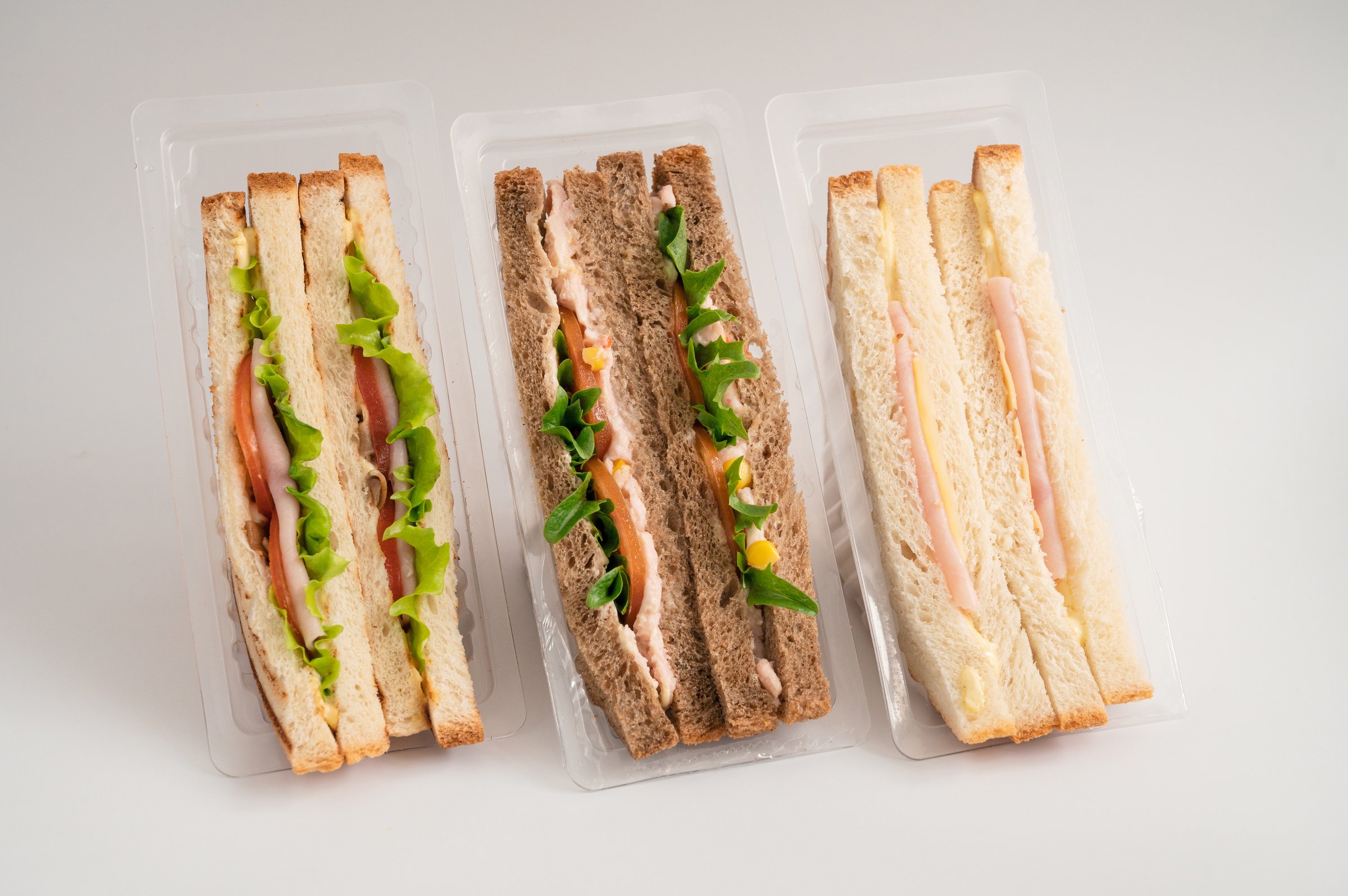Three packaged sandwiches with white and whole wheat bread, filled with lettuce, tomatoes, turkey, cheese, ham and greens. Ideal for quick meals.
